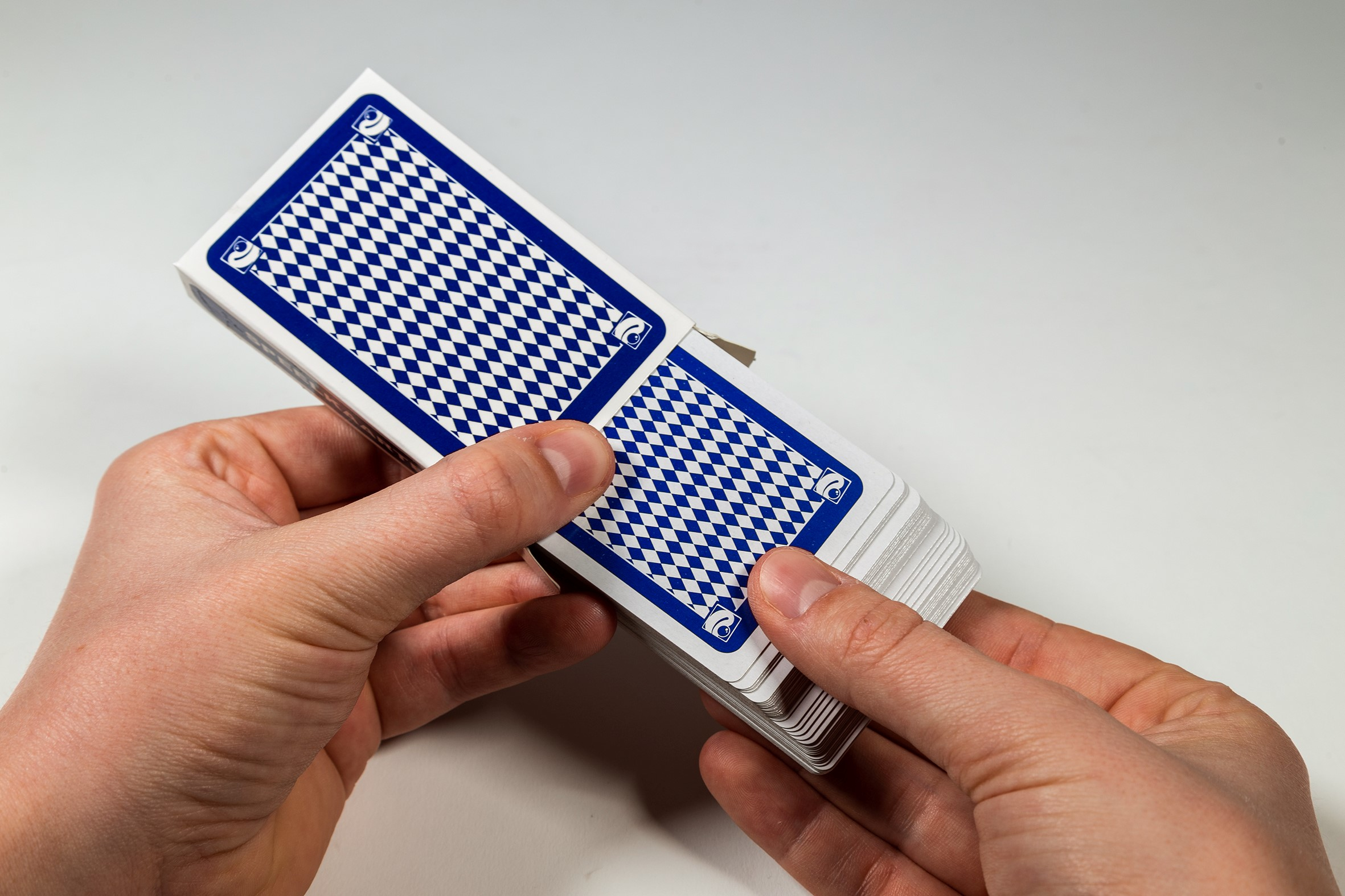 Gros plan de mains tenant un jeu de cartes. Les cartes ont un motif à carreaux bleu au dos.