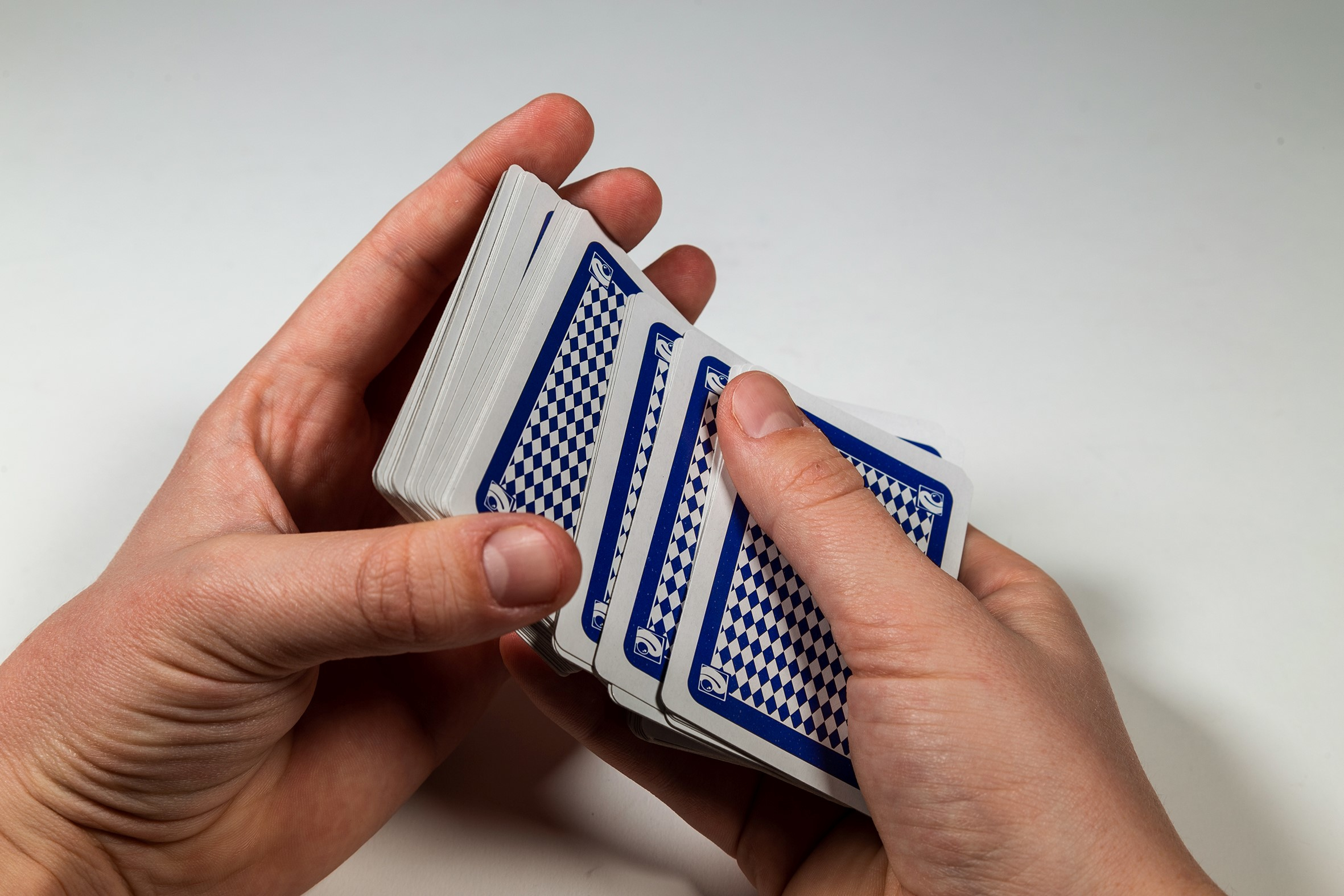 Mains d'une personne tenant un jeu de cartes, légèrement éventail, motif bleu au dos.