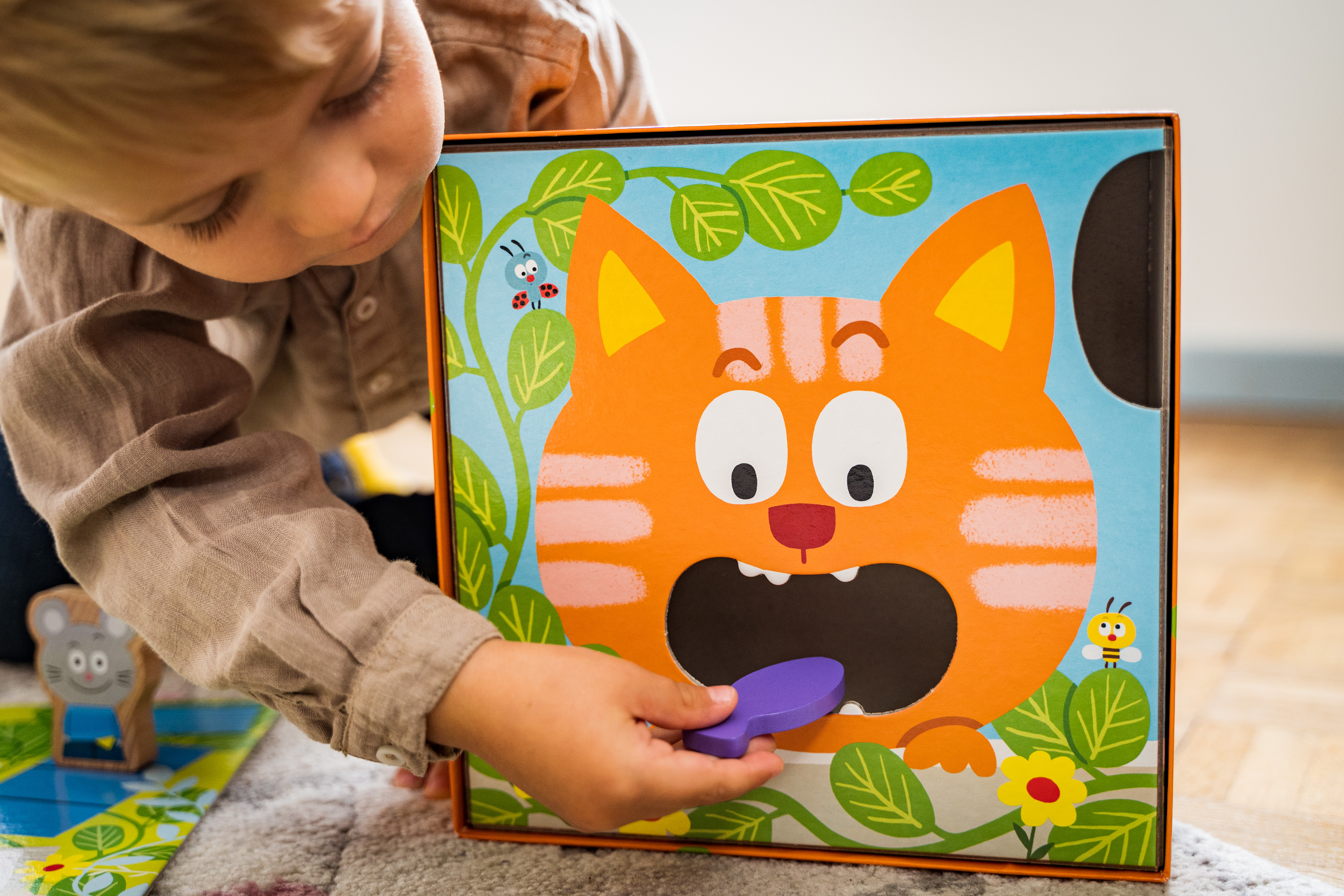 Een kind dat interactie heeft met een houten kattenpuzzel, een paarse vorm invoegt.