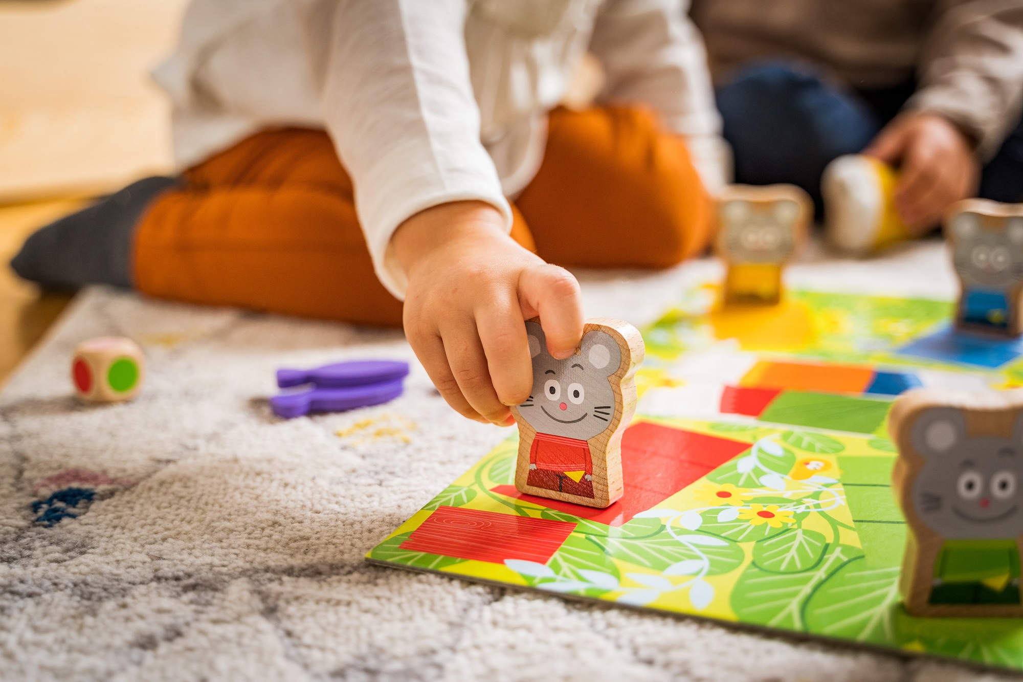 Een kinderhand die naar een houten muisstuk grijpt op een kleurrijk bordspel.