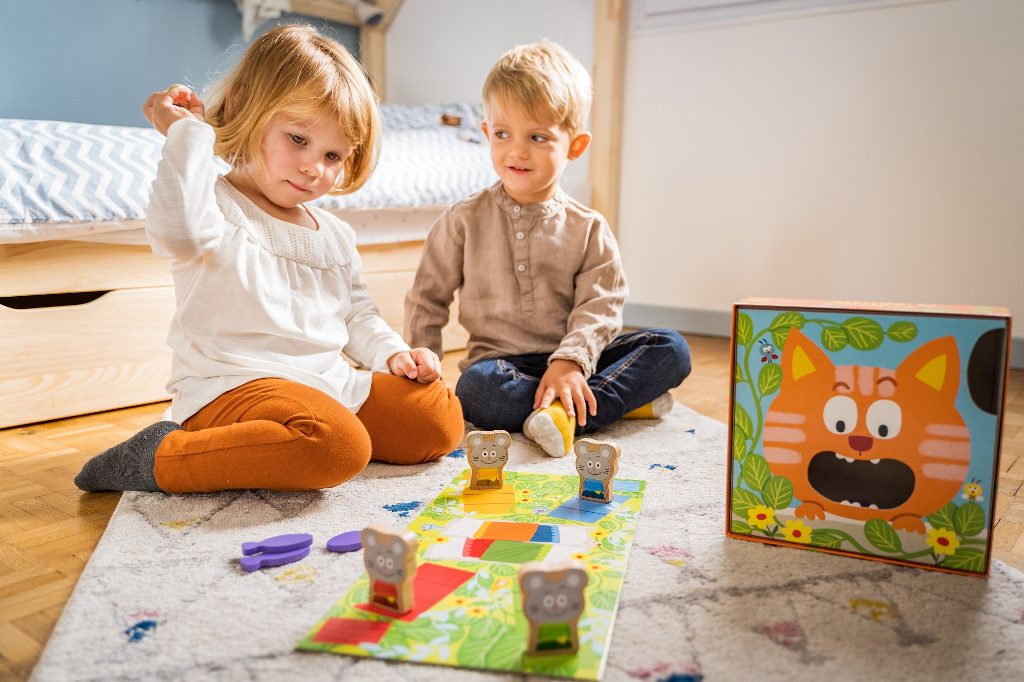 Twee kinderen die een bordspel spelen met houten muisfiguren en een kattenillustratie.