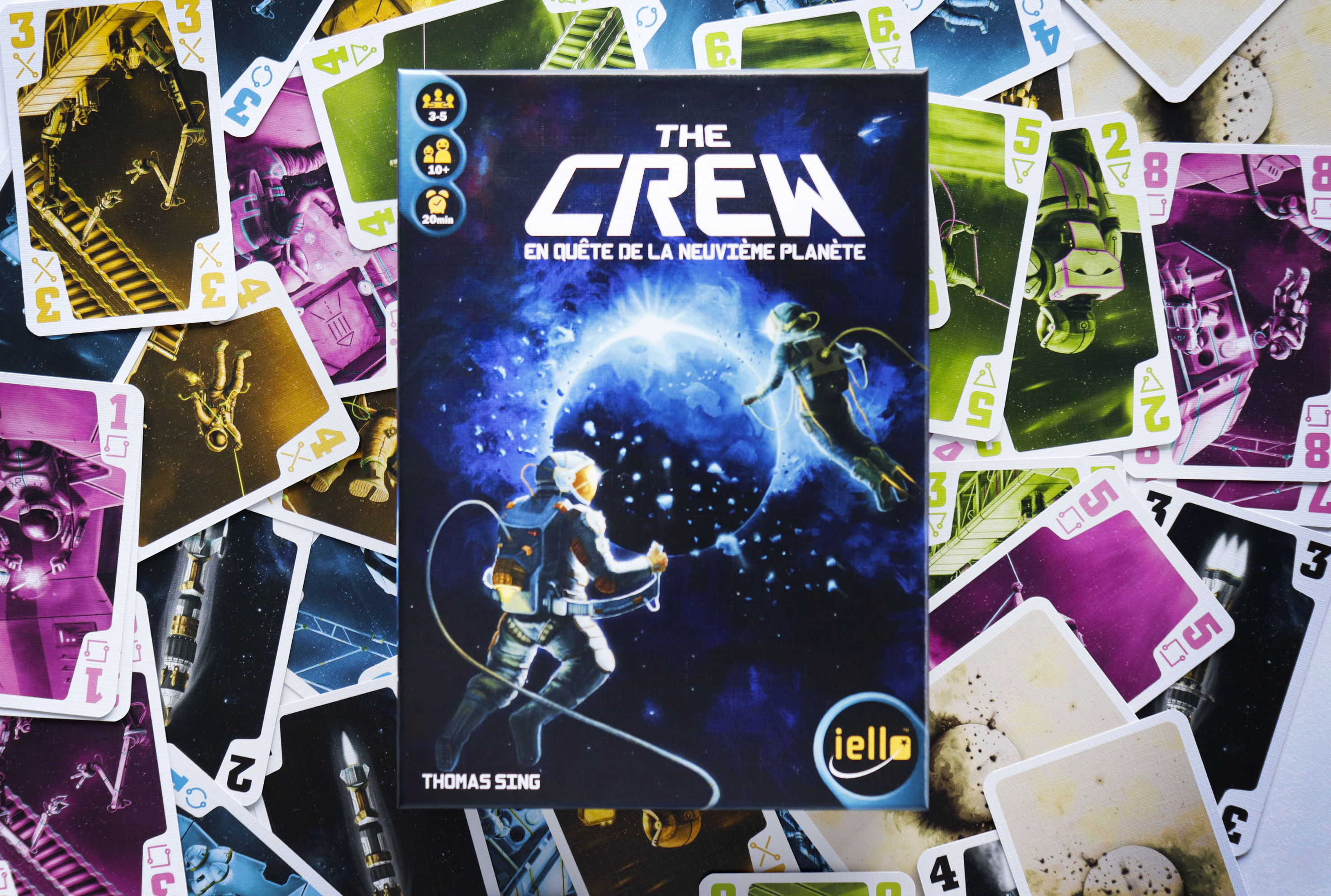 Pudełko gry planszowej 'The Crew' z rozrzuconymi kartami. Przedstawiono astronautów.