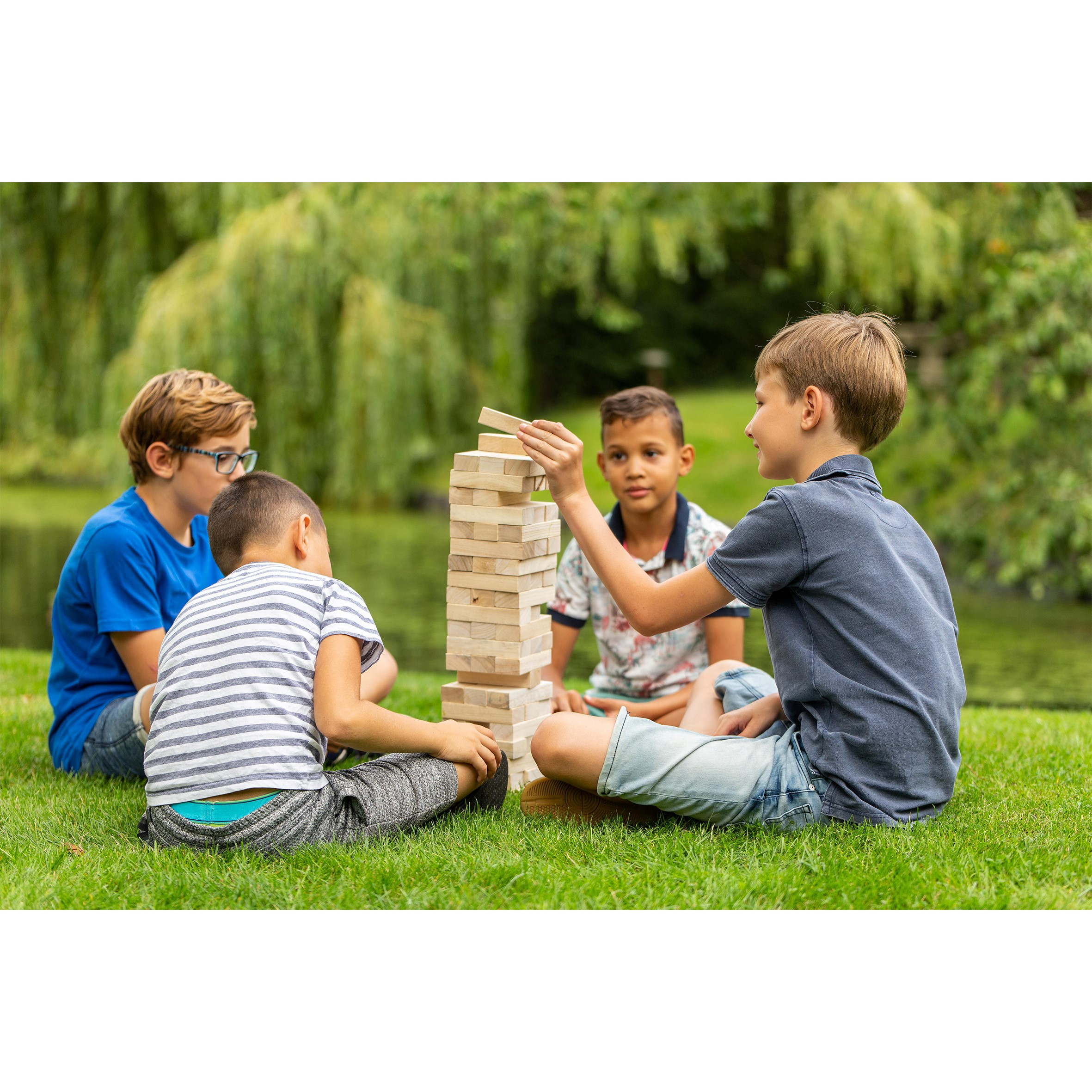 Quattro bambini giocano a Jenga in un giardino con un lago visibile sullo sfondo.