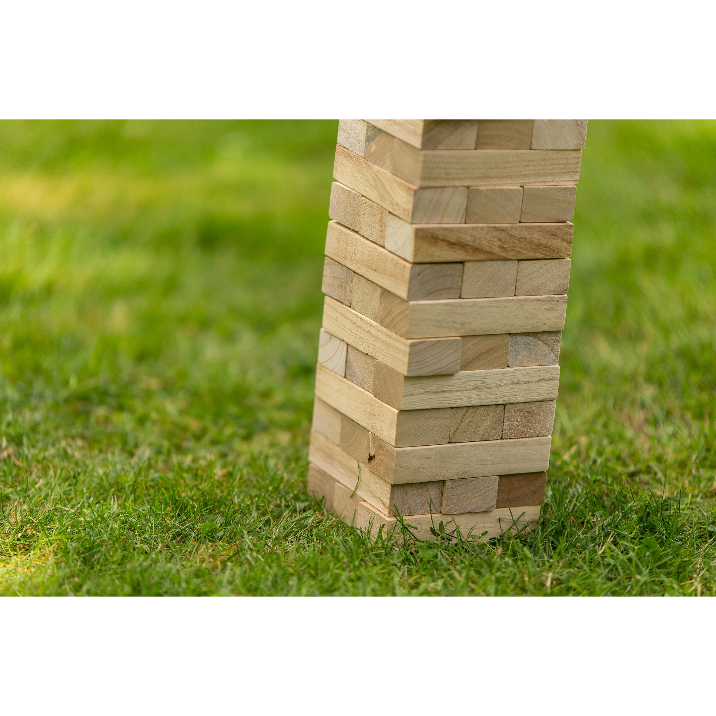 Torre Jenga in legno su erba verde. La torre è parzialmente in vista, leggermente decentrata.