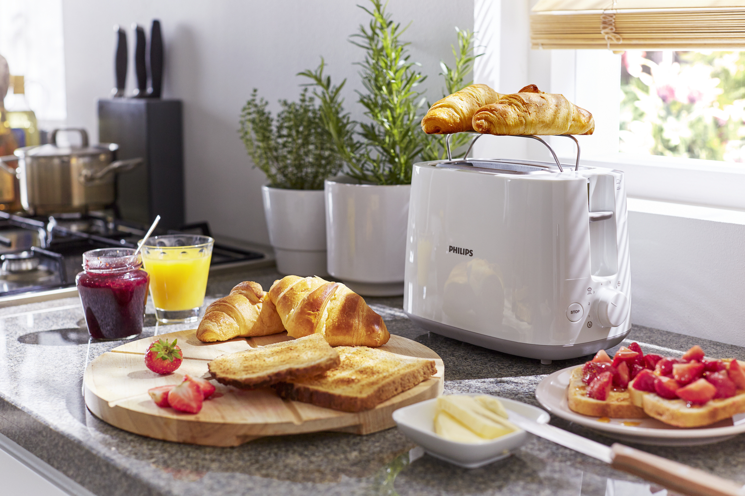 Scena in cucina con tostapane, croissant, toast, succo, marmellata e frutta.