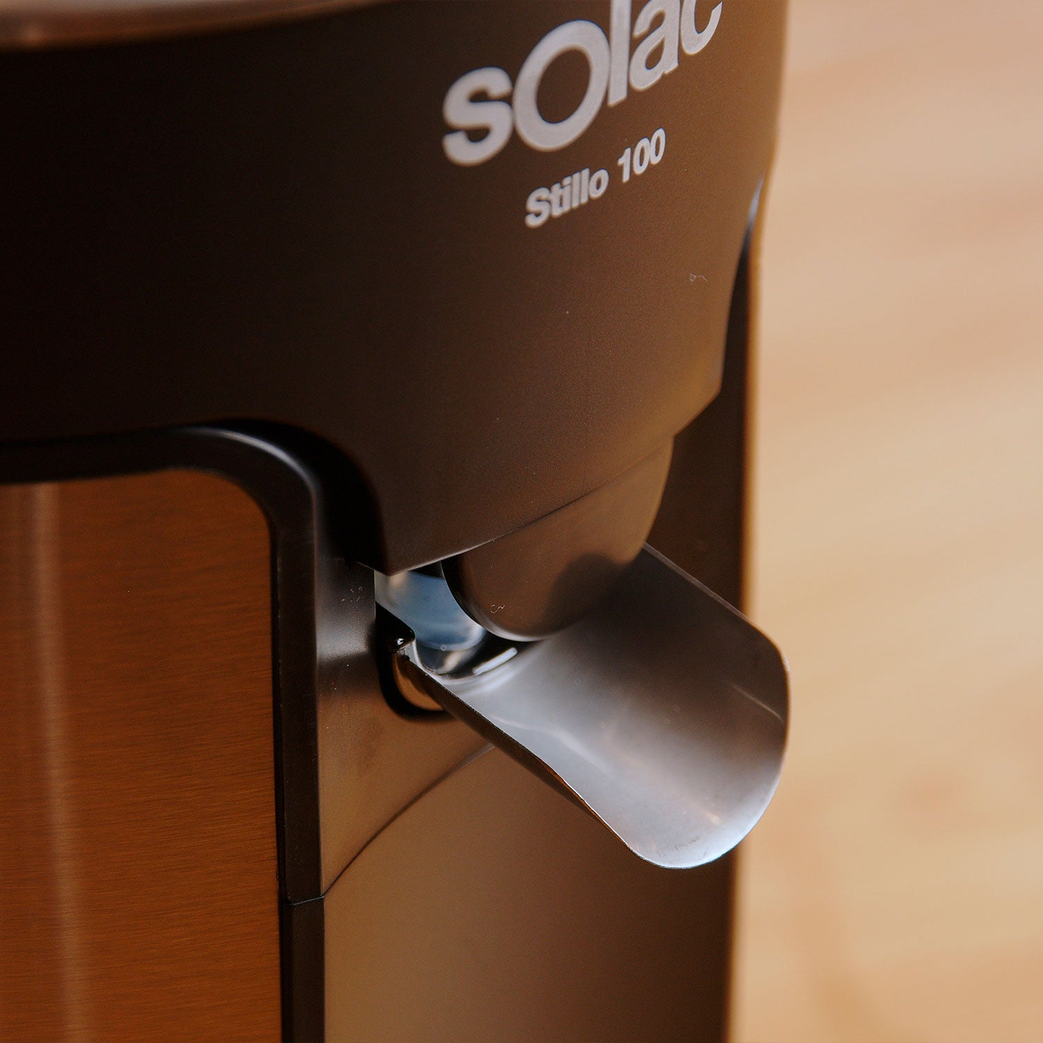 Zbliżenie brązowej i metalicznej wyciskarki z wylewką. Marka to Solac.