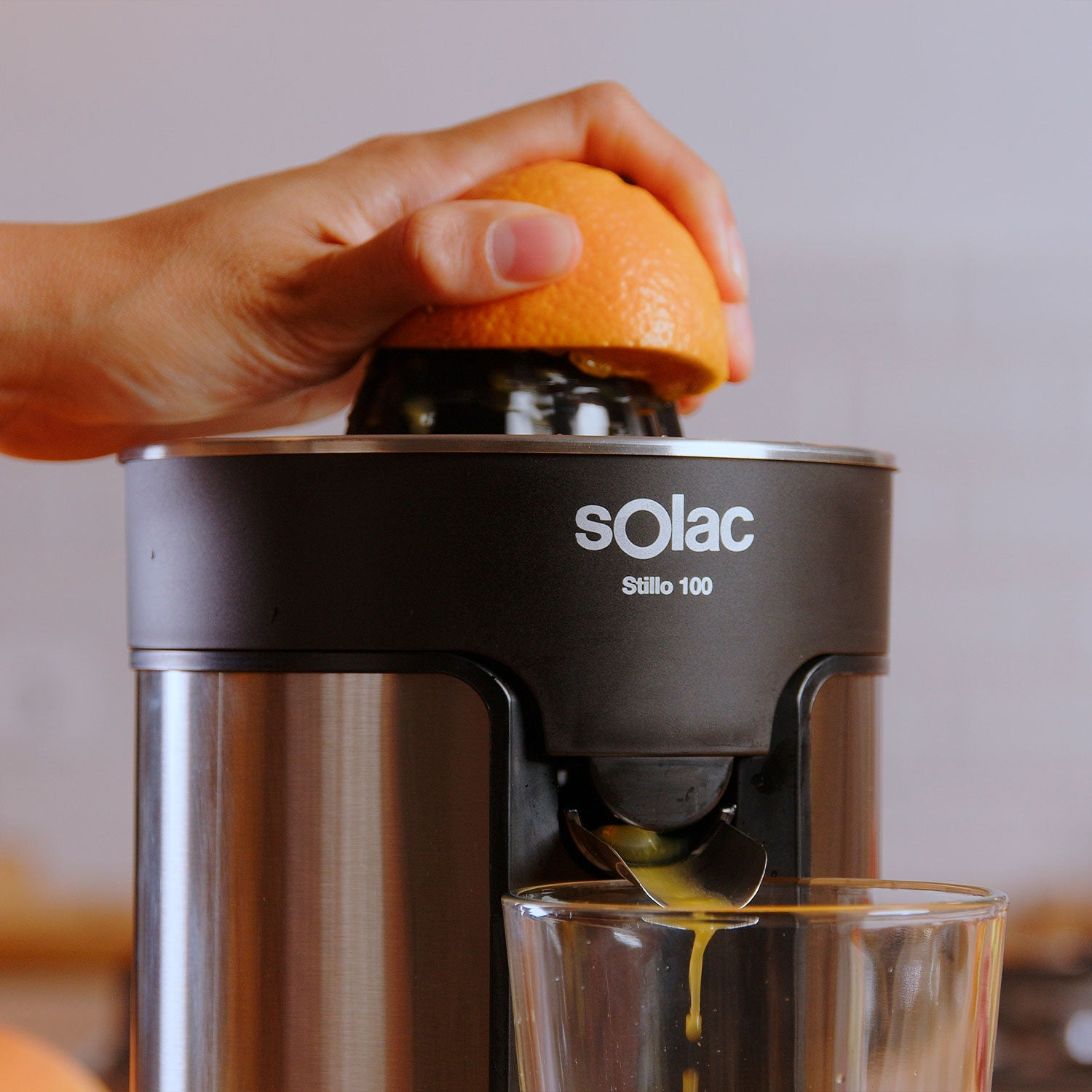 Osoba wyciskająca pomarańczę do wyciskarki Solac. Pod wylewką znajduje się szklanka.