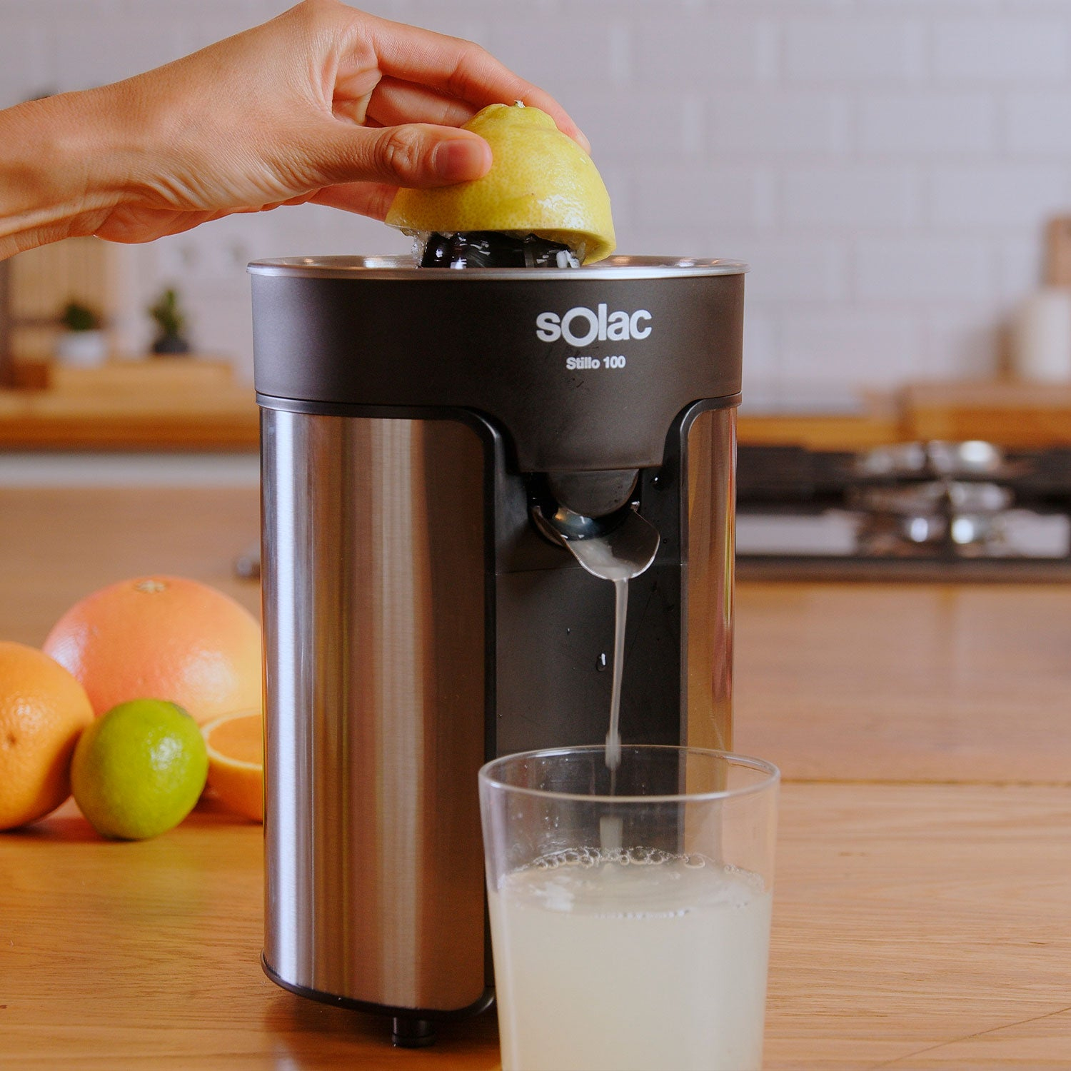 Osoba wyciskająca cytrynę na wyciskarce. Szklanka soku i owoce na drewnianym stole.