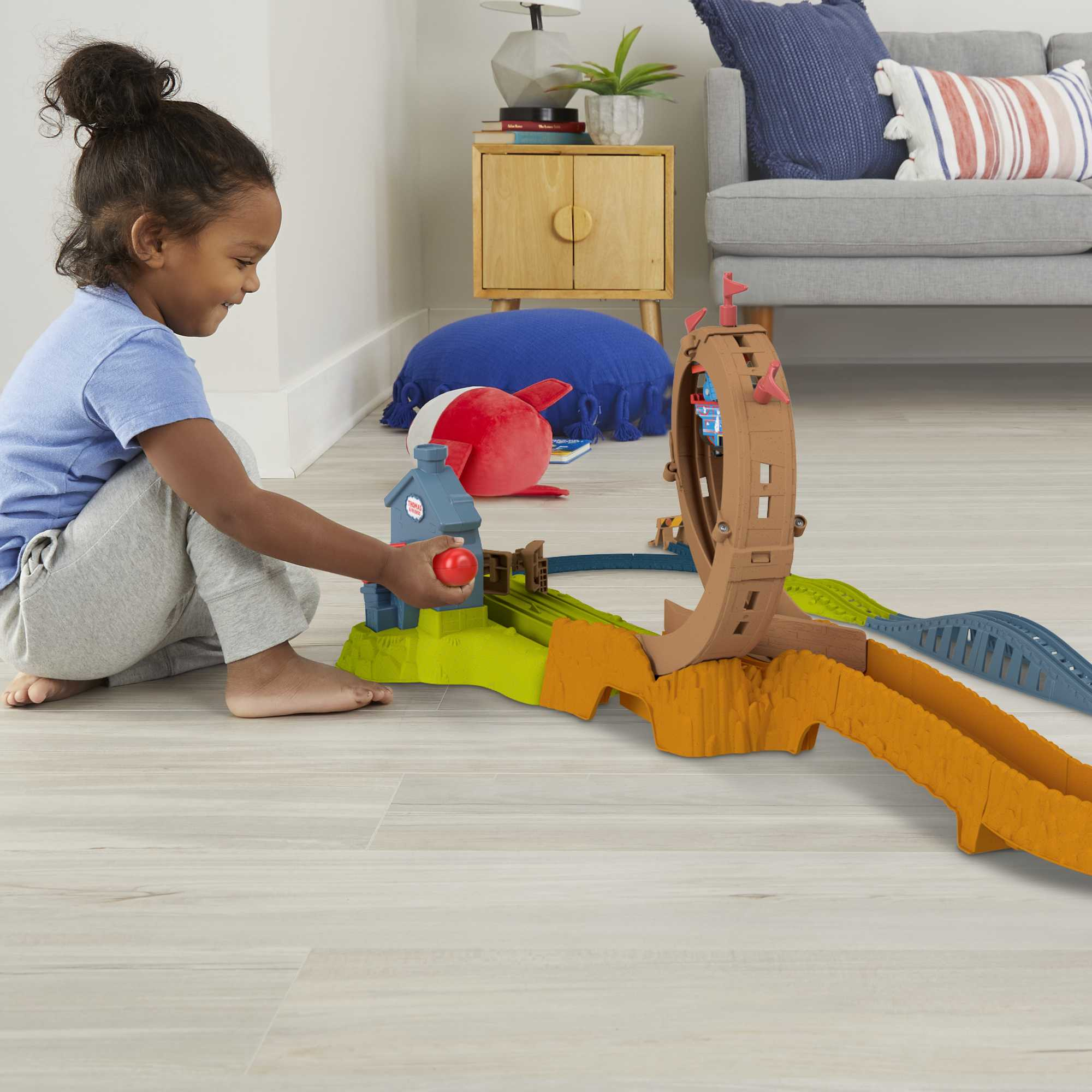 Ein Kind spielt mit einem Thomas & Friends Spielzeug-Zug-Set, in der Nähe eines Hauses und einer Strecke.