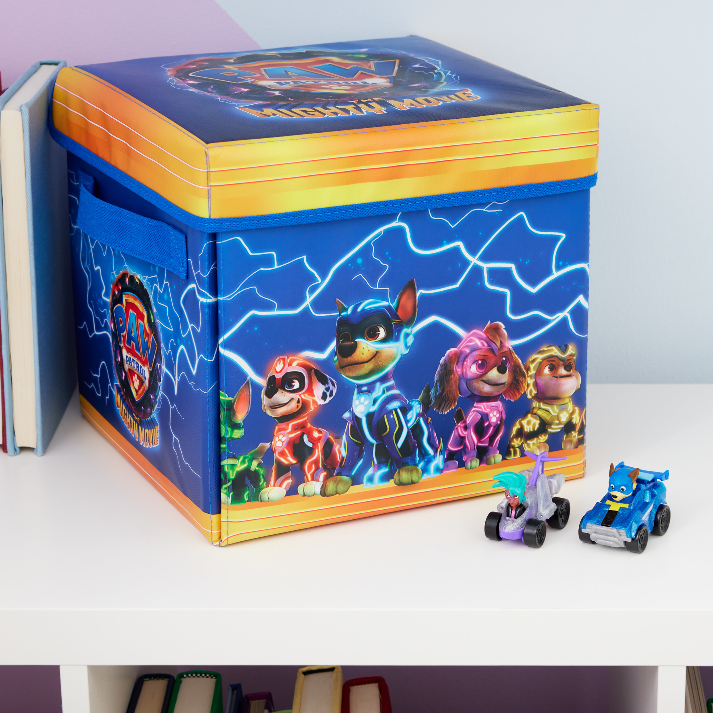 Niebieskie pudełko do przechowywania zabawek Paw Patrol z postaciami z kreskówek. Dwa samochodziki z przodu.