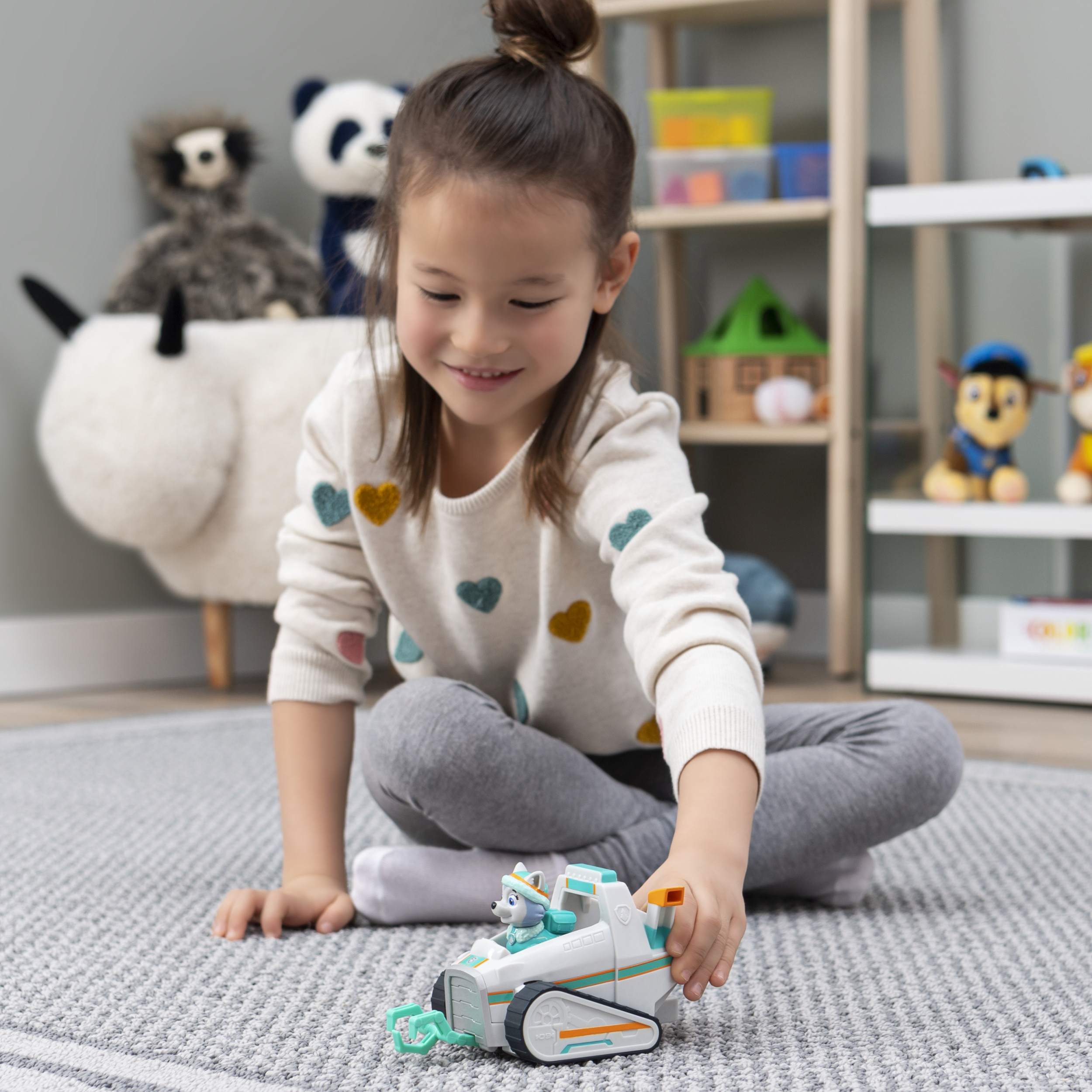 Niña jugando con vehículo de juguete en la alfombra.