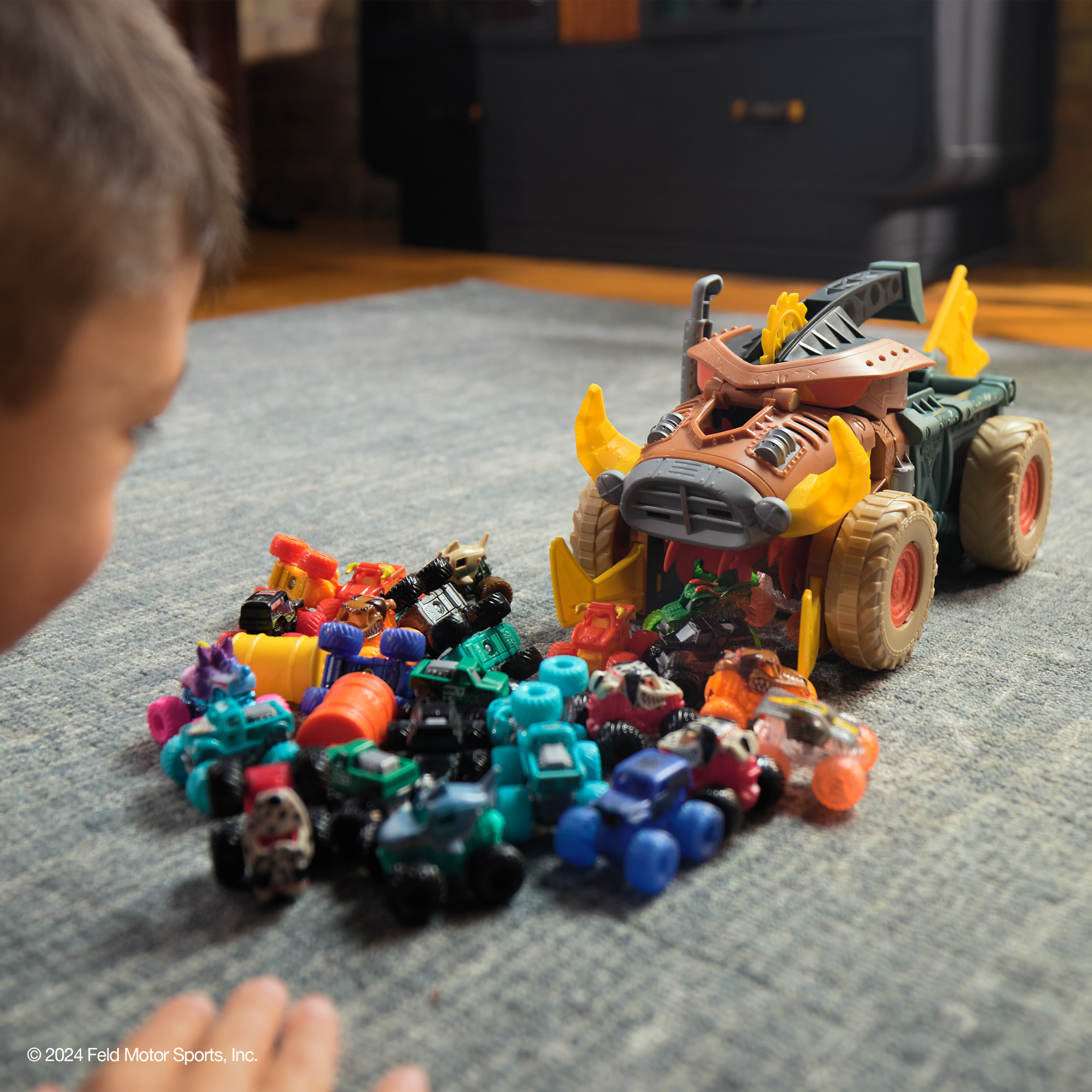 Dziecko patrzy na zabawki monster truck na dywanie.