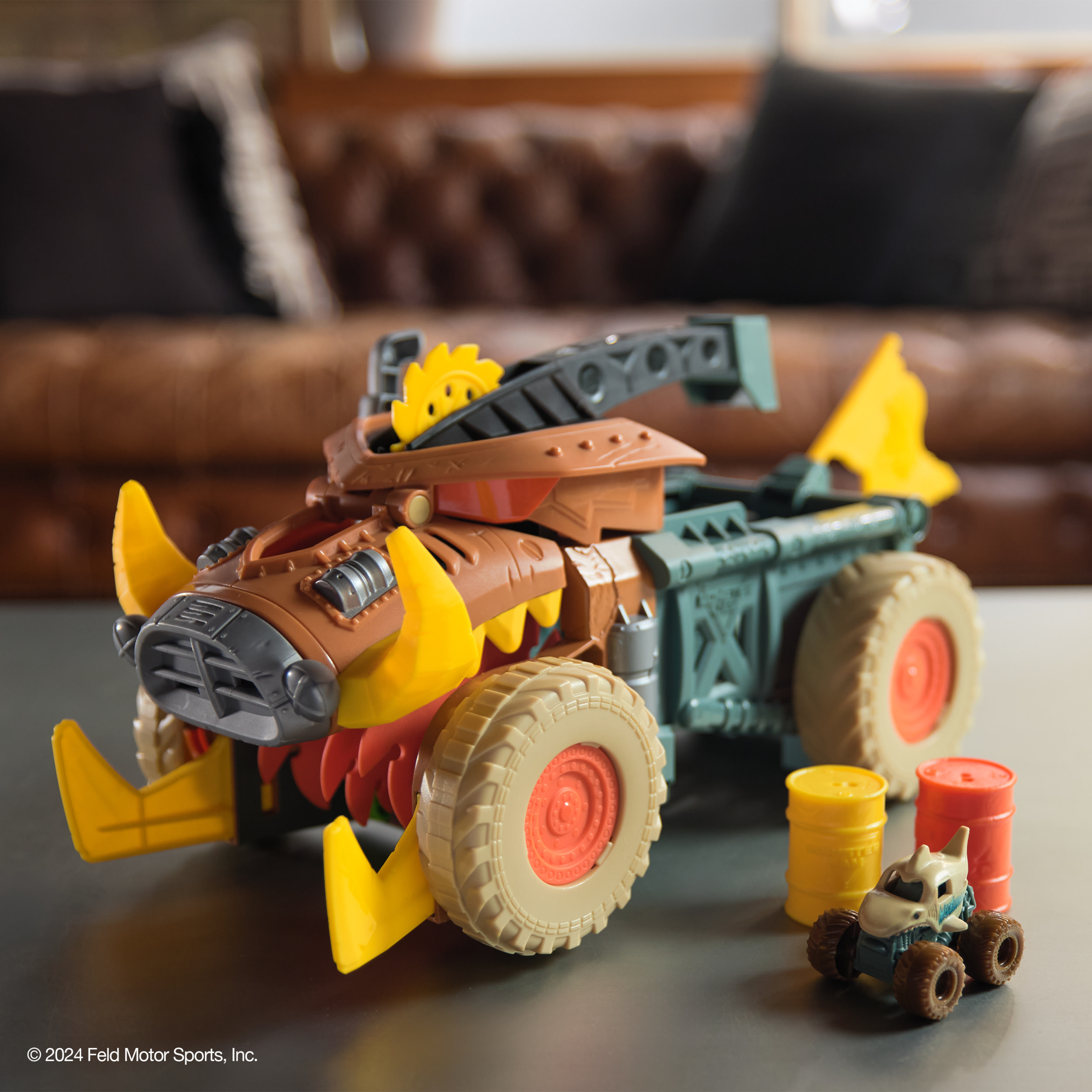 Zabawkowy monster truck na stole. Żółte beczki i mała ciężarówka w pobliżu.