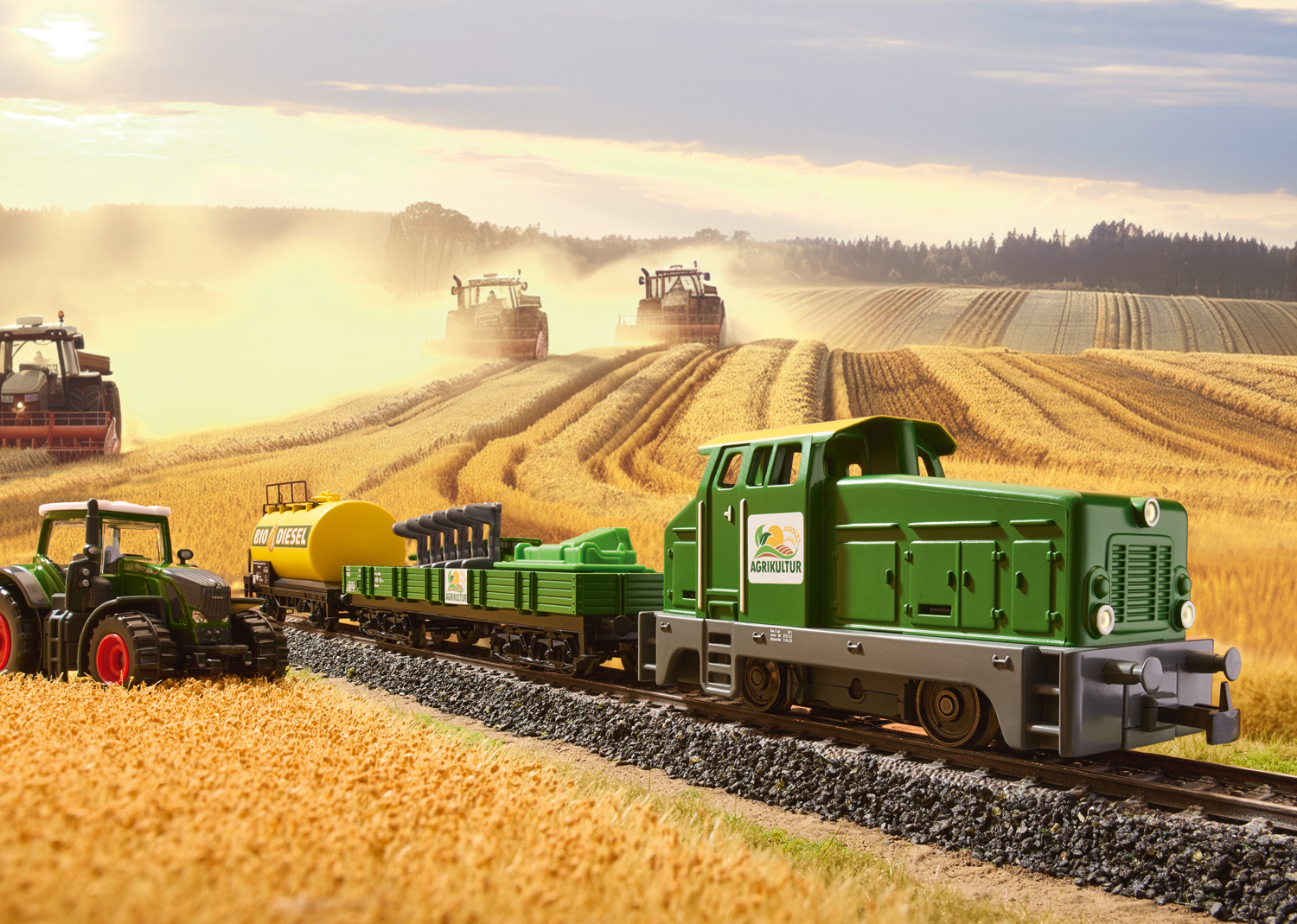 Zielony pociąg zabawka na torach, z polami i traktorami w tle, o zachodzie słońca.