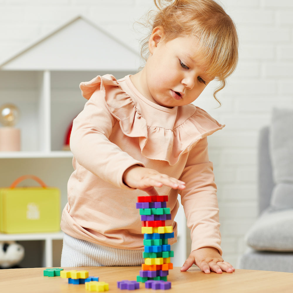 Ein Kind baut einen bunten Blockturm, Blöcke liegen auf dem Boden verstreut.