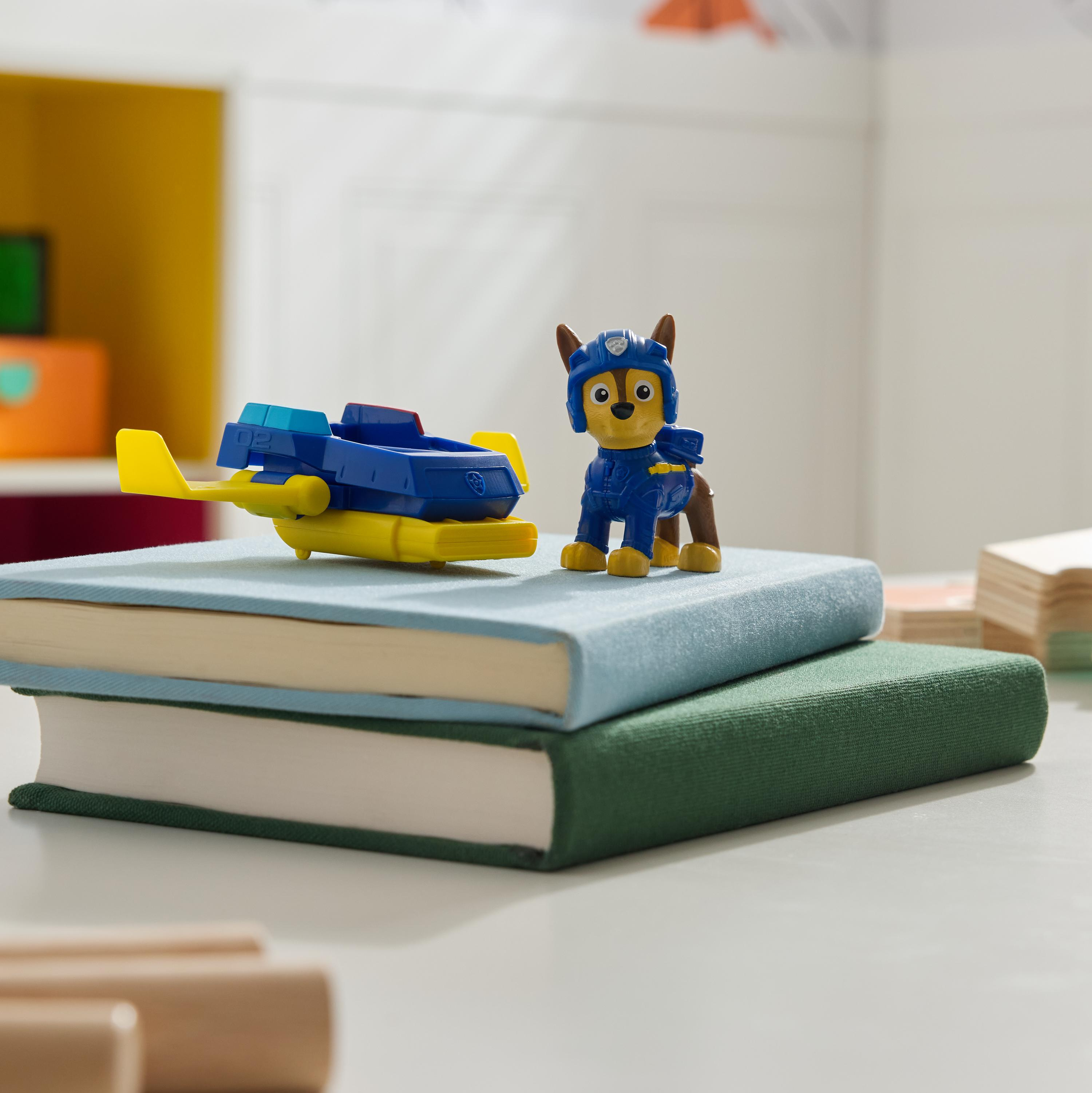 Ein Paw Patrol Spielzeug und ein blaues Flugzeug liegen auf Büchern. Die Szene ist auf einem weißen Tisch.