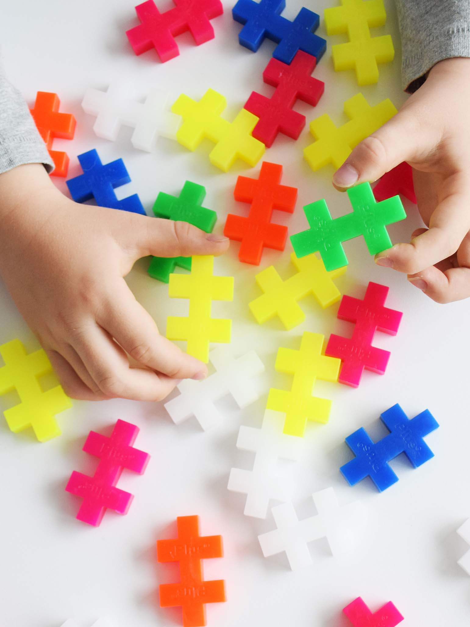 Hände spielen mit bunten, plusförmigen Bausteinen auf weißer Oberfläche.