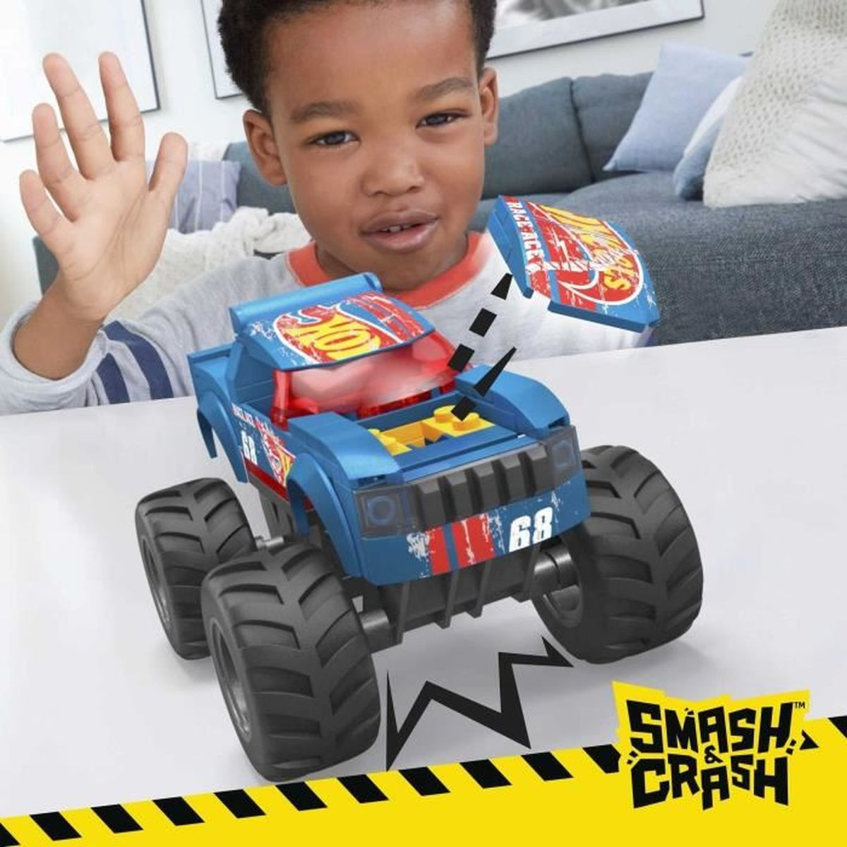 Un bambino gioca con un camion mostro giocattolo blu. Un cartello rosso e il logo Smash & Crash sono in vista.