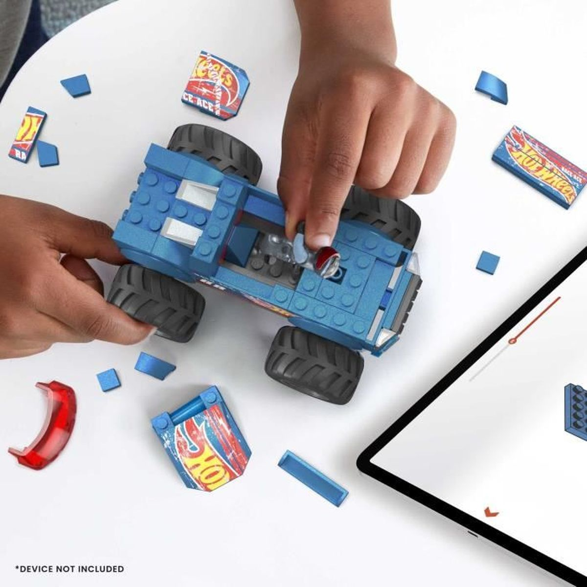 Una persona che assembla un camion mostro giocattolo blu. Ci sono pezzi sparsi e un tablet è visibile.
