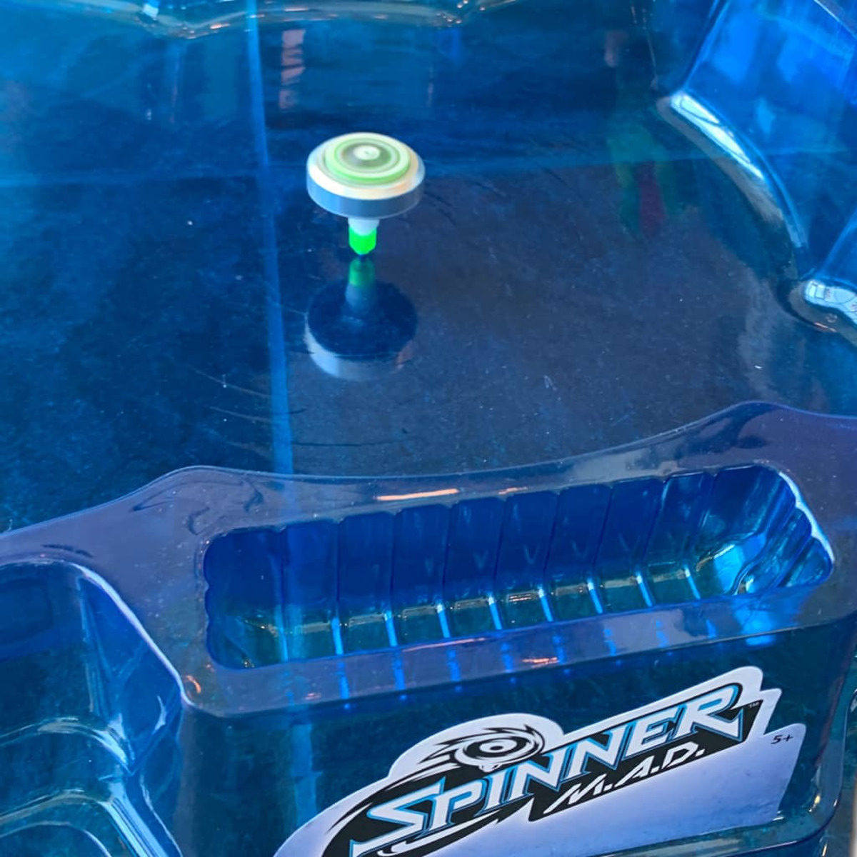 Wirujący wierzchołek na niebieskiej arenie. Arena ma czarno-białe logo.