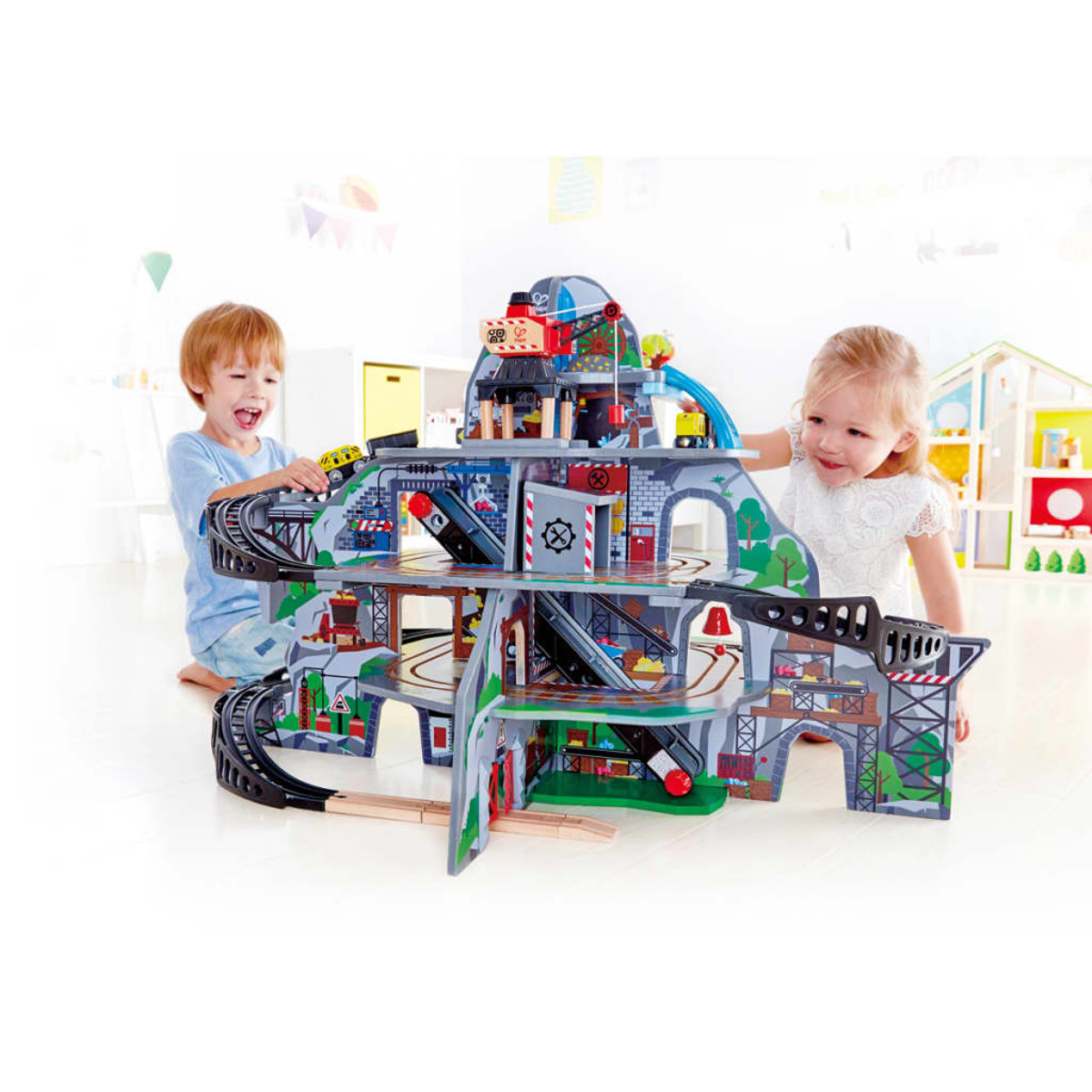 Dzieci bawią się drewnianym zestawem kolejowym. Zestaw zawiera tunele, tory i most.