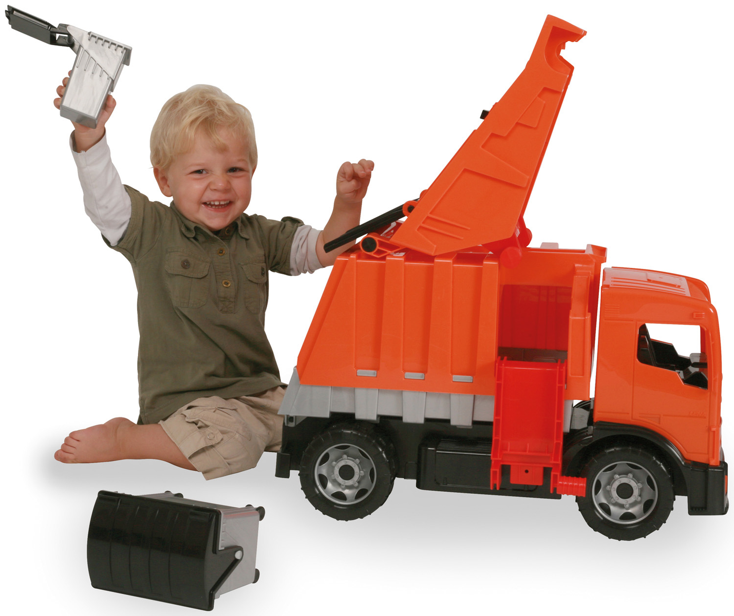 Ein kleiner Junge spielt mit einem Spielzeug-Müllwagen, hält ein Teil davon in der Luft und lächelt.