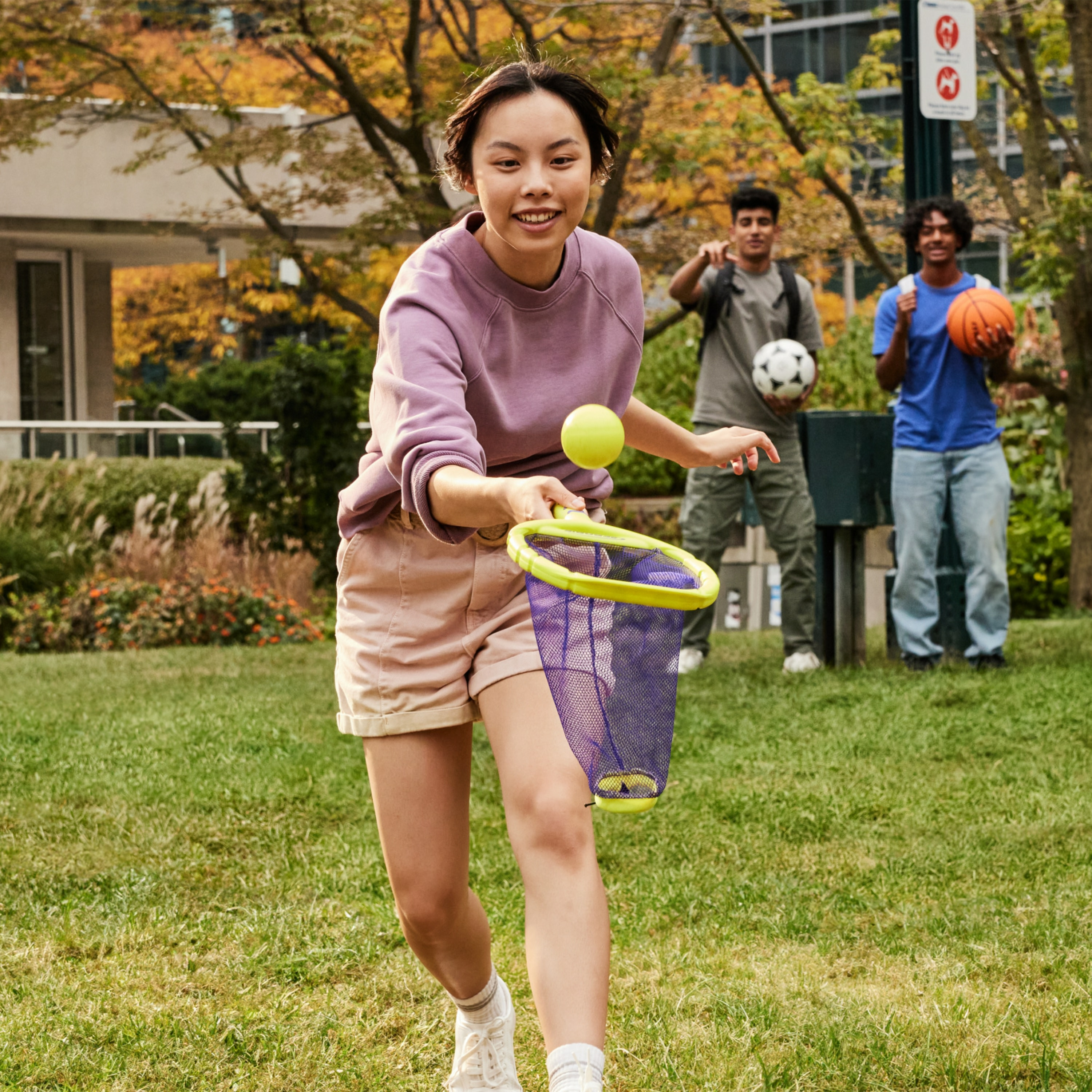 Kobieta gra żółtą piłką, w tle dwóch mężczyzn.