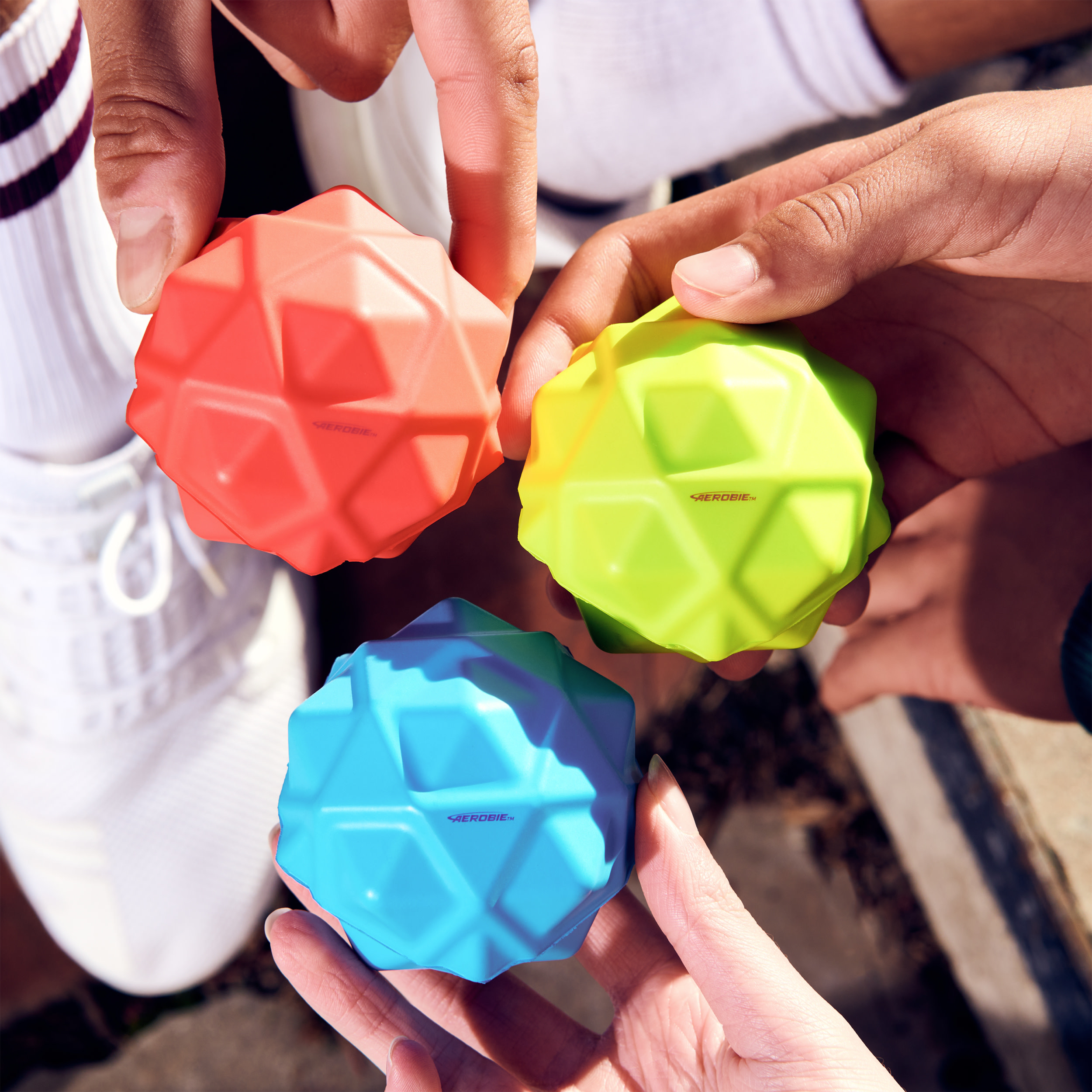 Trzy wielokolorowe, fasetowane piłki Aerobie trzymane w dłoniach.