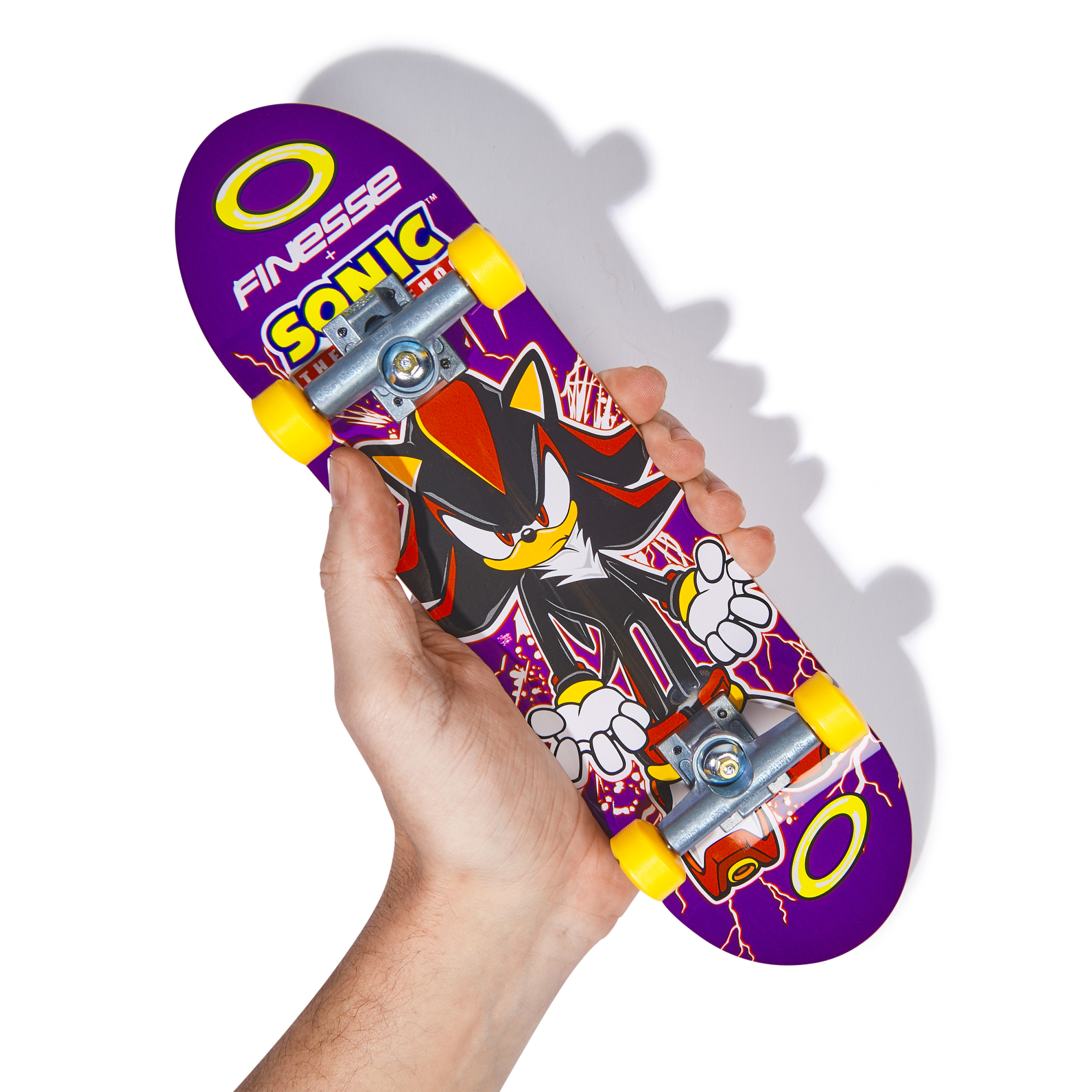 Dłoń trzymająca deskorolkę Tech Deck z grafiką Shadow the Hedgehog. Fioletowe i czerwone kolory.