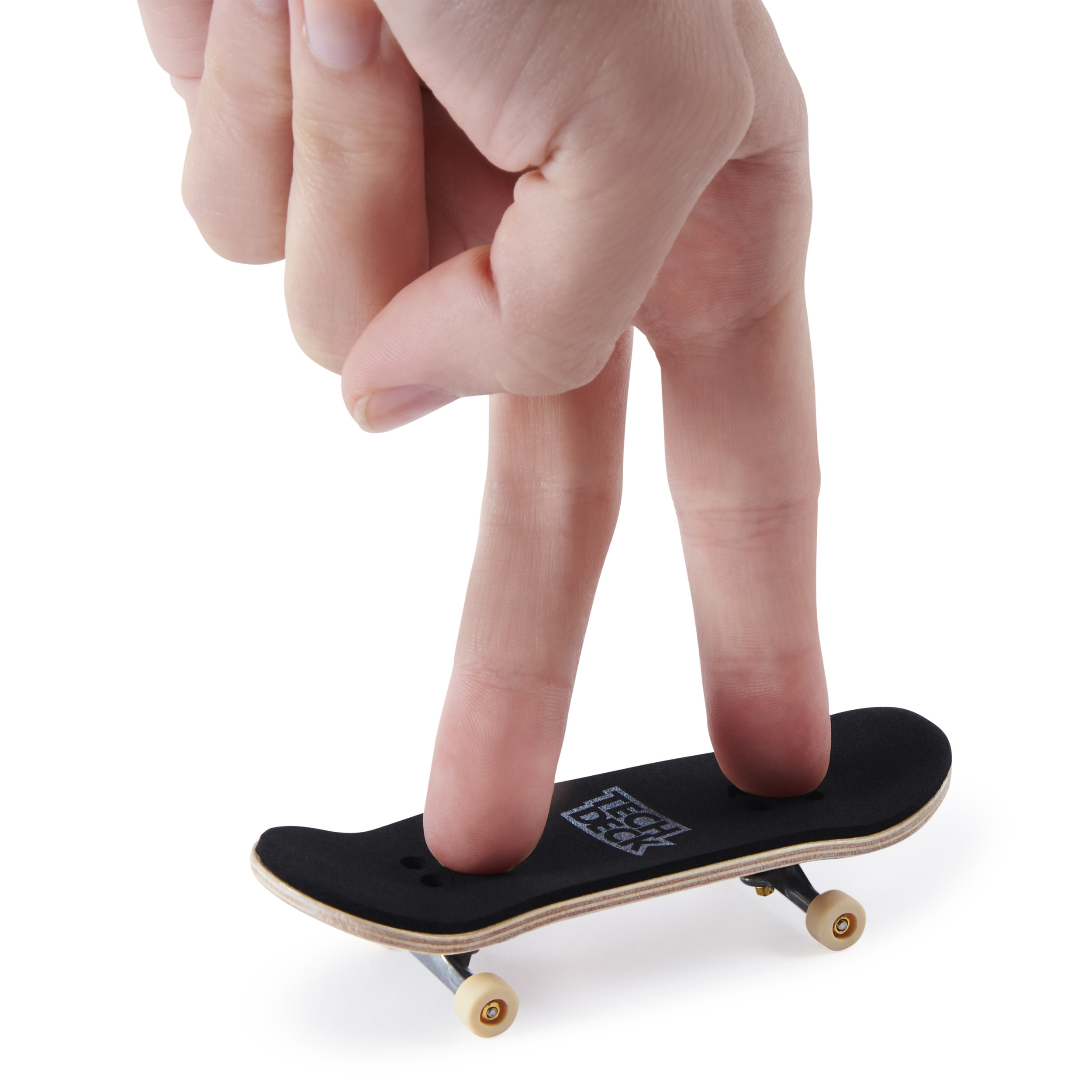 Palce równoważą małą czarną deskorolkę Tech Deck na białym tle.