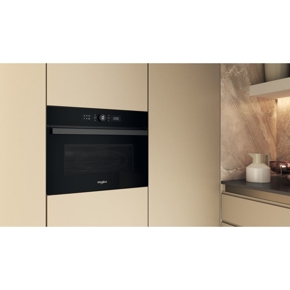 Un horno microondas negro empotrado en un entorno de cocina beige. La puerta del horno está cerrada.
