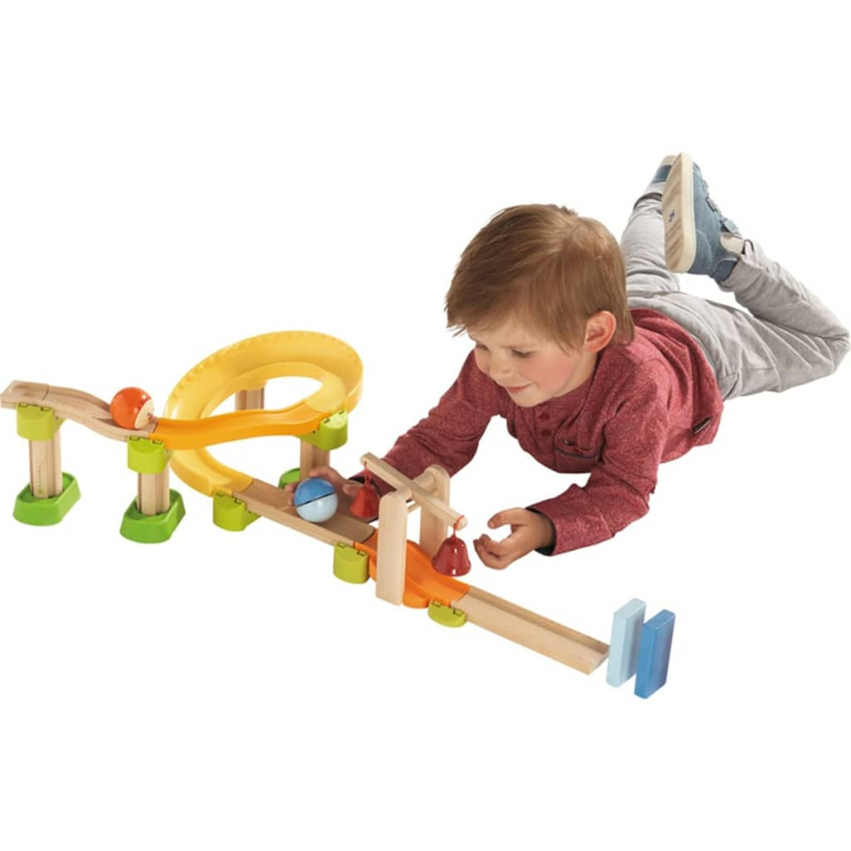 Ein kleiner Junge spielt mit einer Holzspielzeugbahn. Die Bahn hat Kugeln, eine Rutsche und eine Glocke.