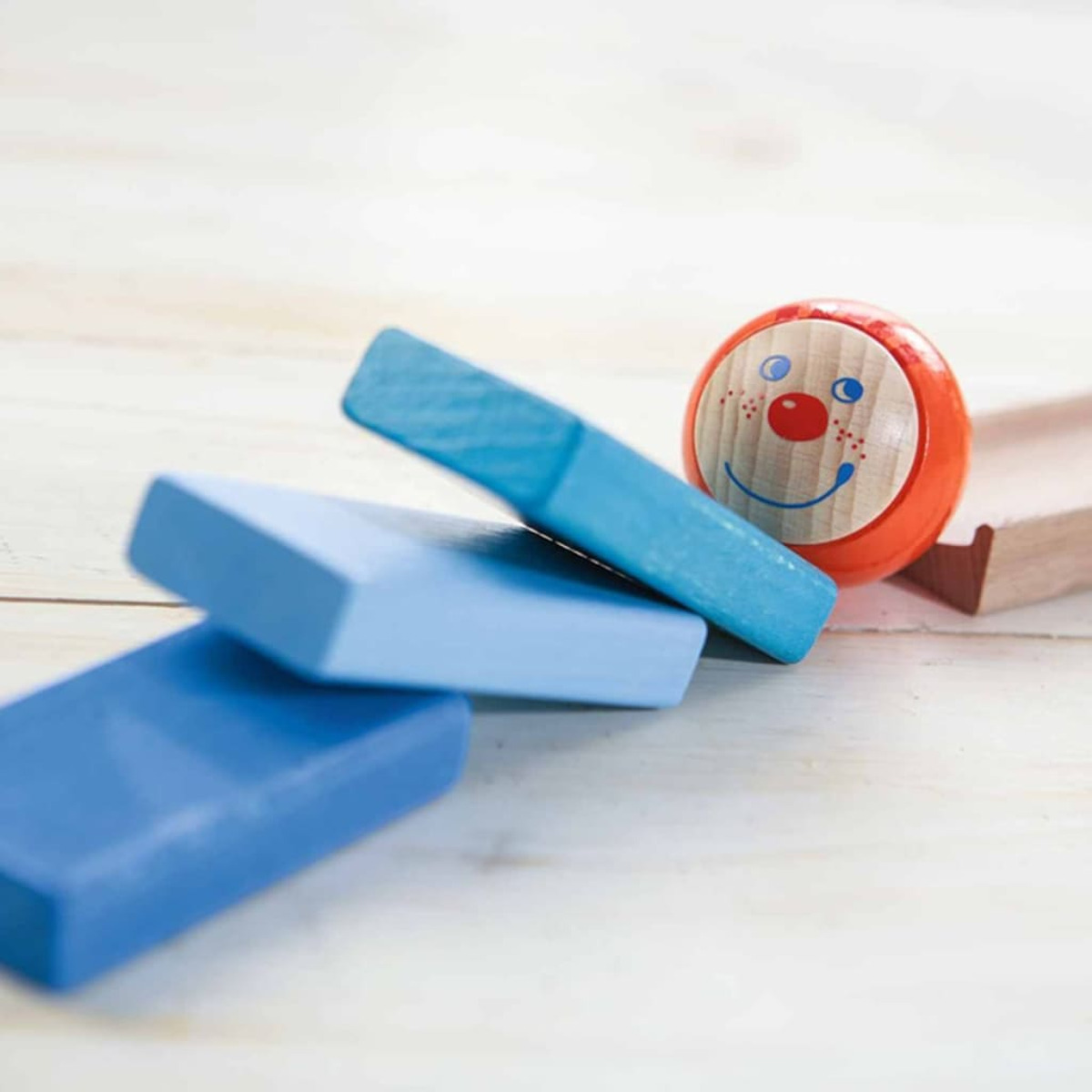 Ein Holzspielzeug mit blauen Blöcken und einem Ball mit Clown-Gesicht. Der Ball ist orange mit roter Nase.
