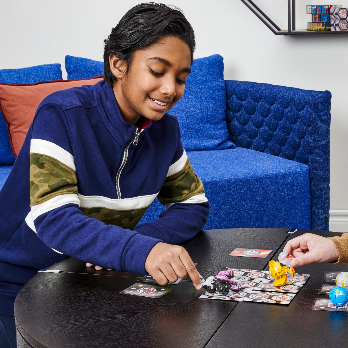 Chłopiec grający w grę Bakugan z kartami i zabawkami na czarnym stole.