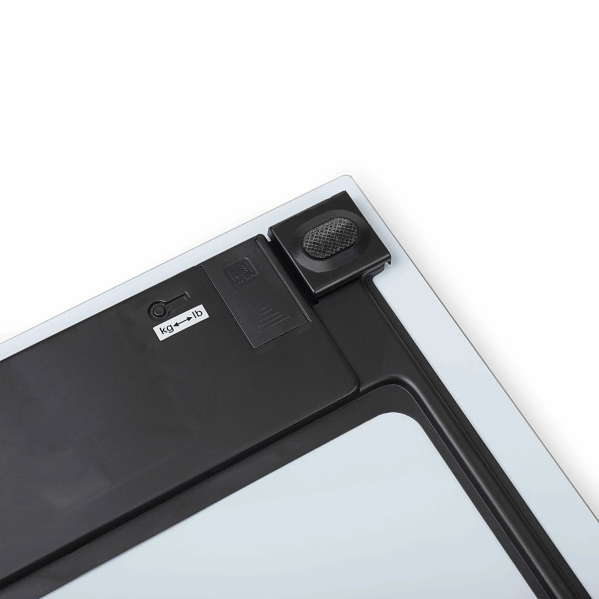Gros plan du dessous d'une balance avec le compartiment de la batterie ouvert. L'étiquette affiche kg et lb.