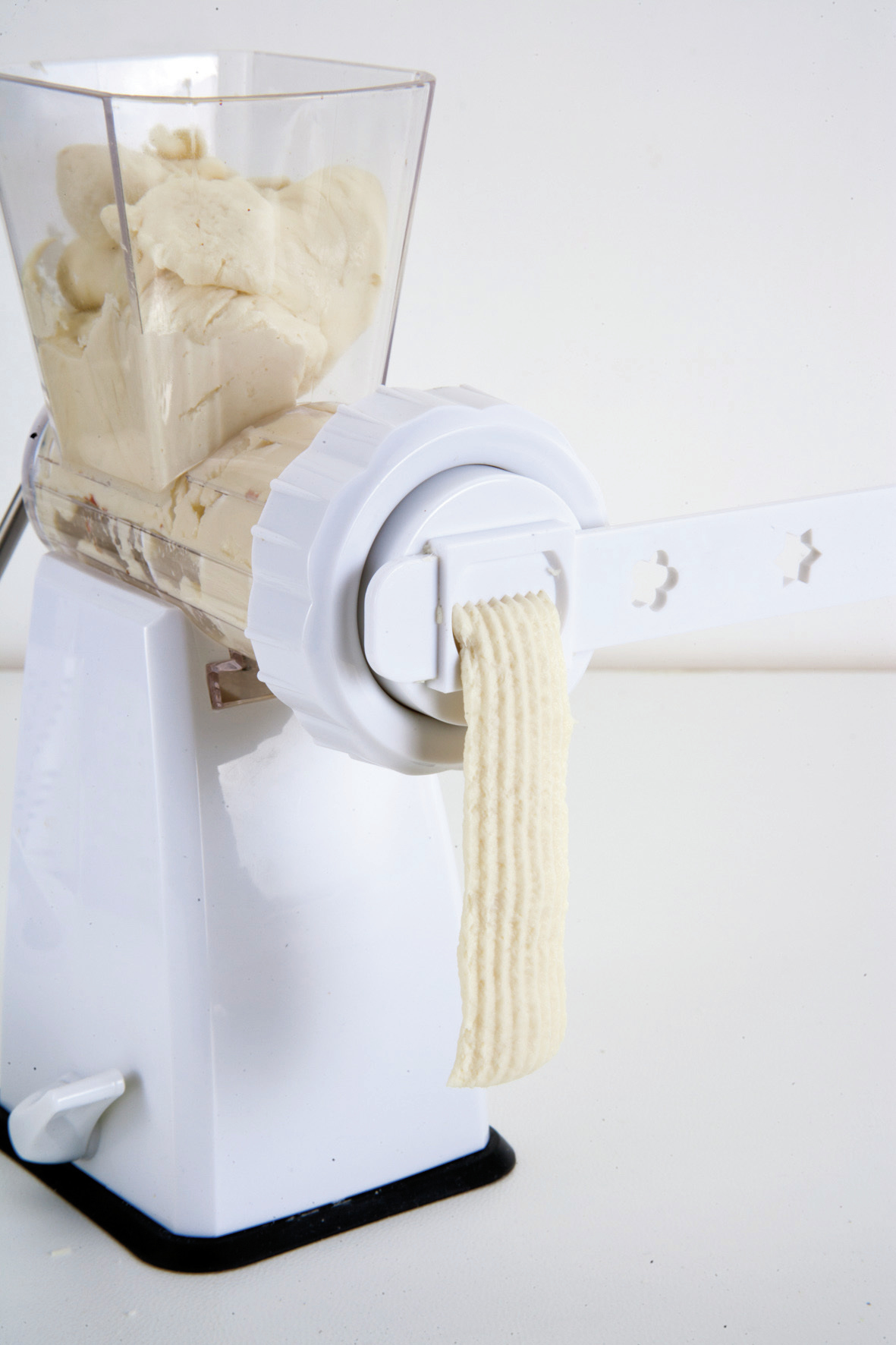 Maszynka do mięsa wyciska materiał przypominający ciasto. Białe tło.