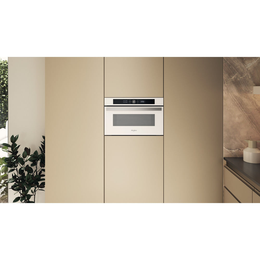 Un forno a microonde da incasso con finiture beige, posto in una cucina con mobili beige.