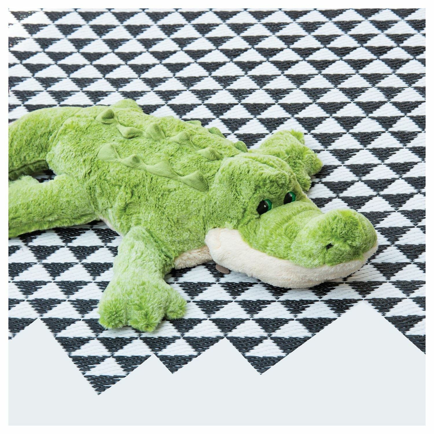 Ein grünes Stoffkrokodil-Spielzeug liegt auf einer schwarz-weißen, geometrisch gemusterten Oberfläche.