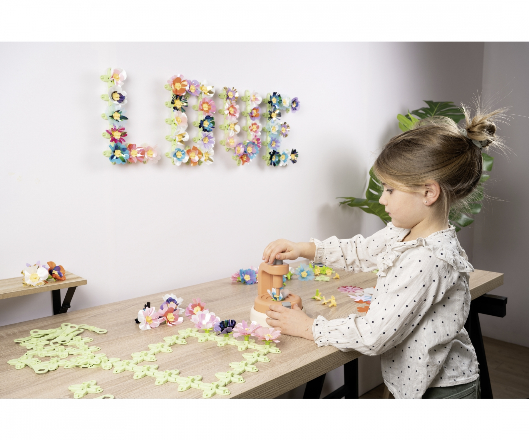 Dziecko robi kwiaty za pomocą maszyny do rękodzieła. Słowo "LOVE" jest napisane na ścianie z kwiatów.