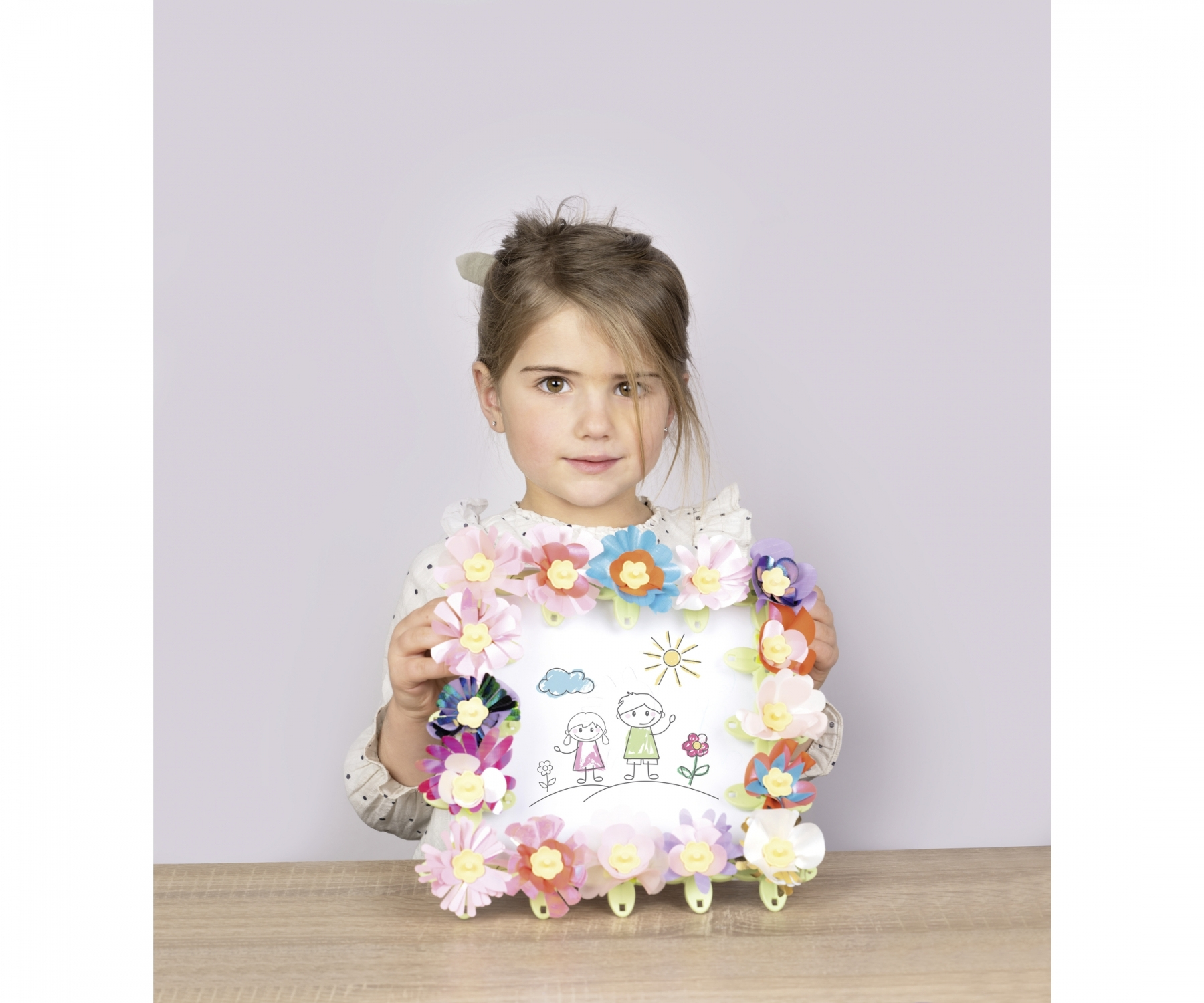 Dziecko trzymające ozdobioną ramkę z kolorowymi papierowymi kwiatami.