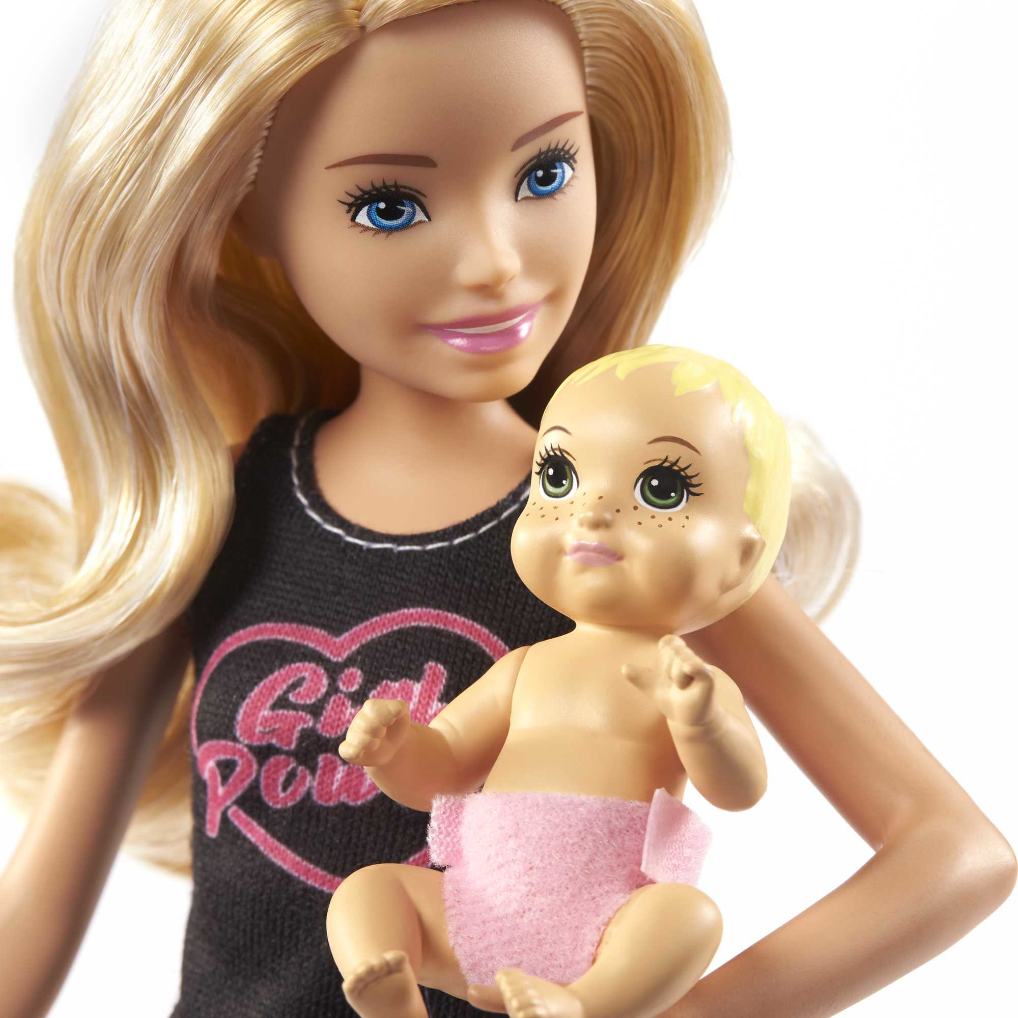 Bambola Barbie bionda che tiene in braccio una bambola. Barbie indossa un top nero con un cuore rosa. Sfondo bianco.