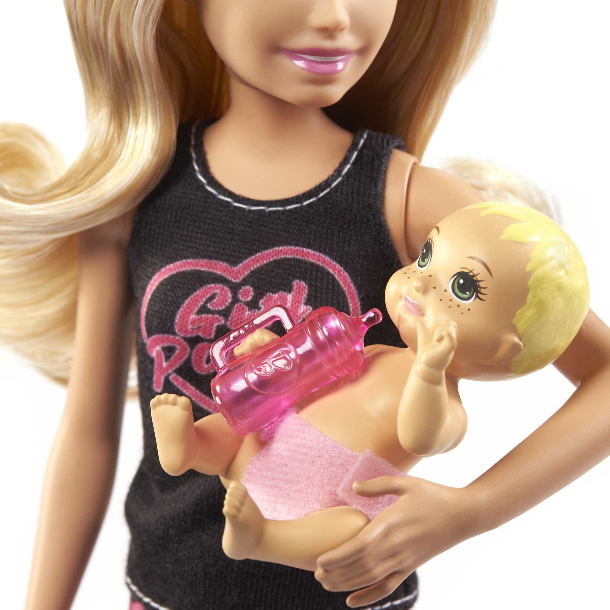 Eine Puppe hält eine Babypuppe mit einer Flasche. Die Puppe trägt ein schwarzes Top. Das Baby trägt eine rosa Windel.