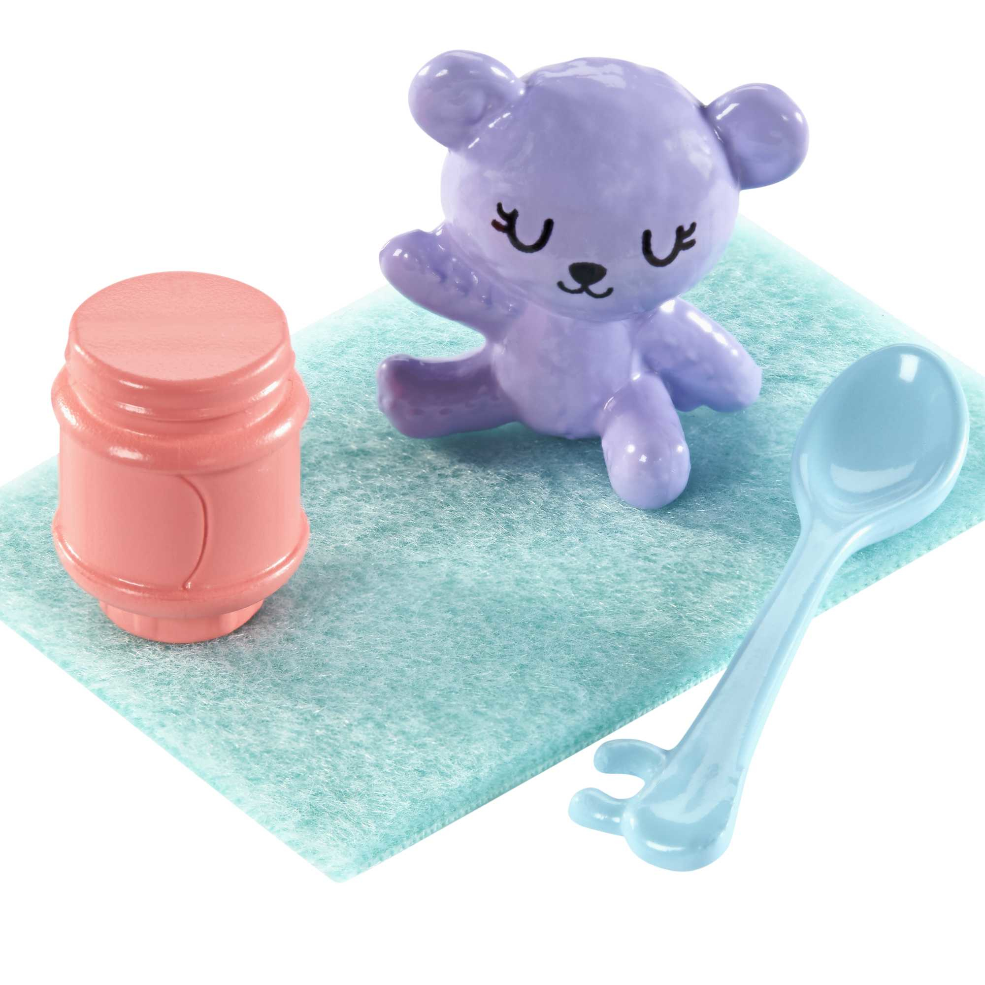 Ein lila Bär-Spielzeug, eine rosa Flasche und ein blauer Löffel, alles auf einem hellblauen Filzquadrat.