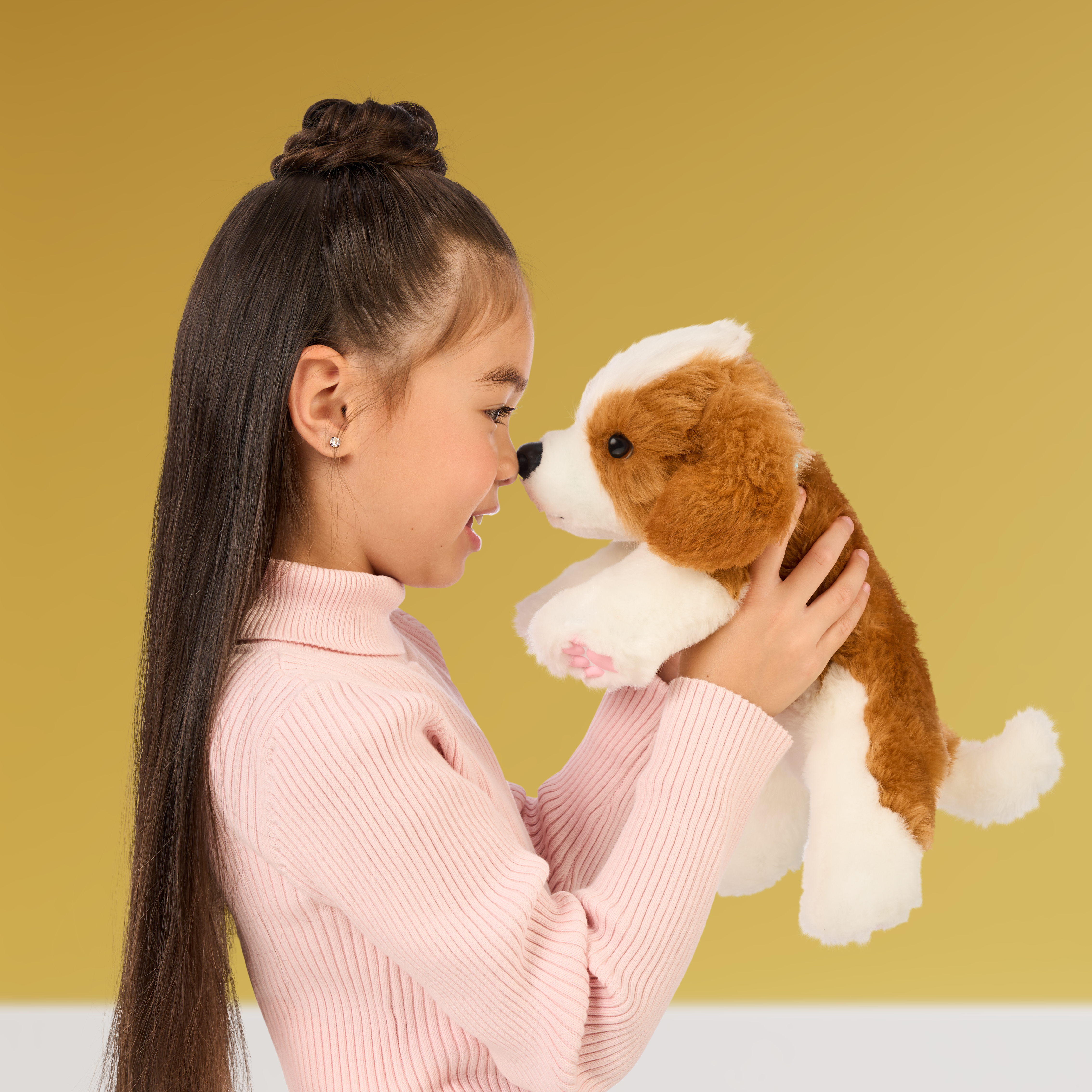 Młoda dziewczyna patrzy na brązowo-białą zabawkę psa, różowa koszula i żółte tło.