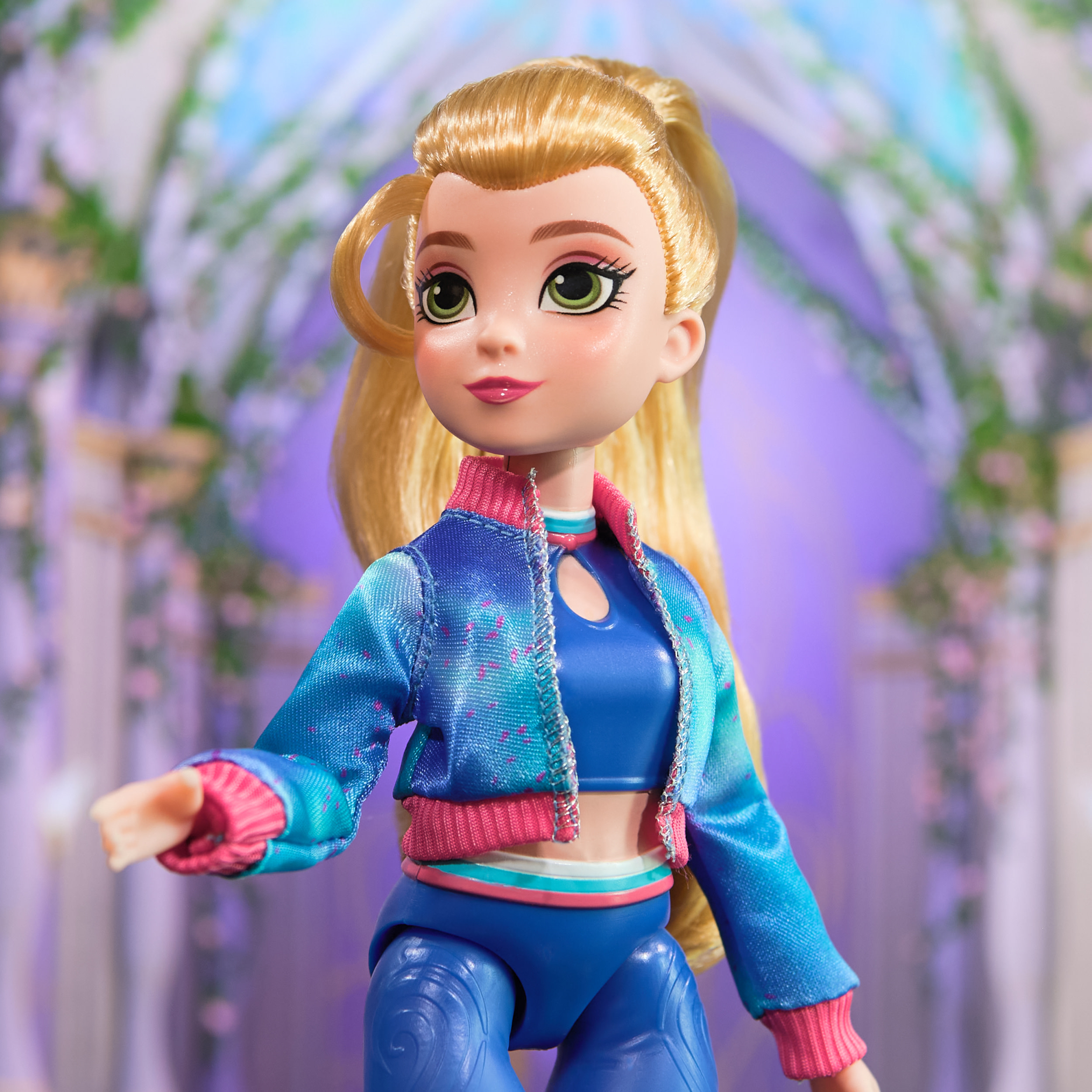 Una muñeca con cabello rubio, que usa una chaqueta y pantalones azules. El fondo es floral y morado.