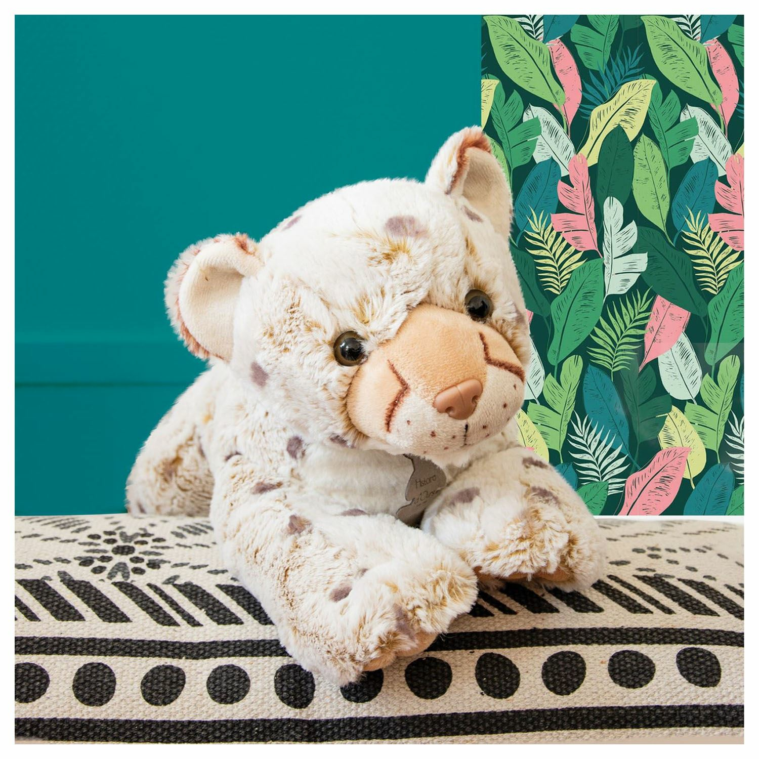 Cętkowany pluszowy lampart na wzorzystej poduszce, z turkusową ścianą i tłem z tapetą w dżunglę.