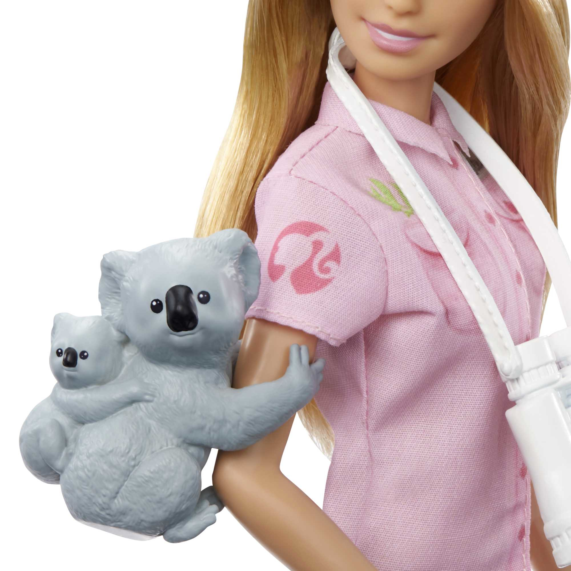 Barbie-Puppe mit rosa Hemd, die einen Koala mit einem kleineren Koala auf dem Rücken hält.