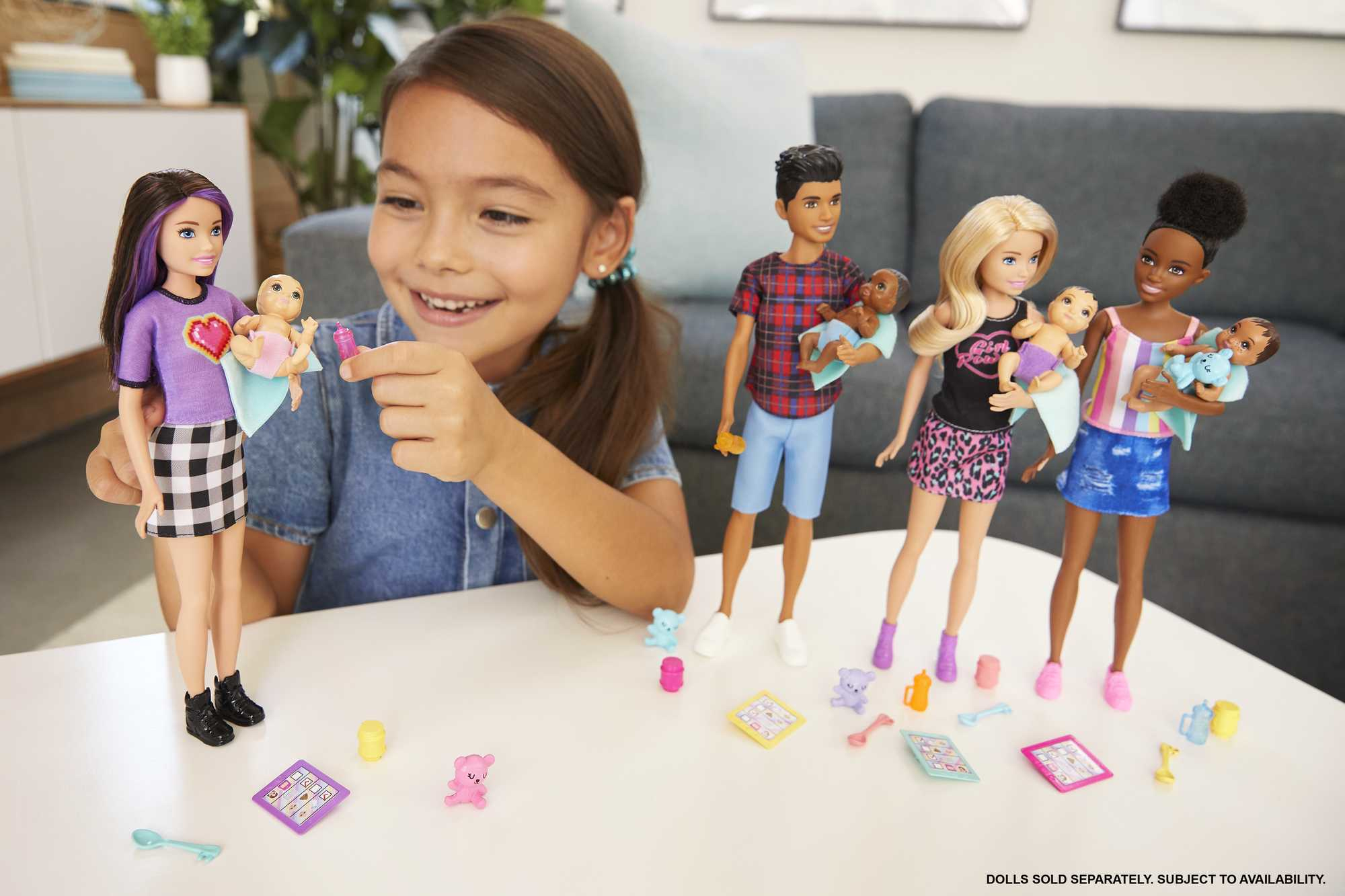Una bambina gioca con bambole e accessori Barbie. Altre bambole e accessori sono sul tavolo.