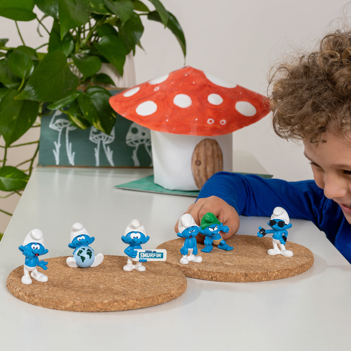 Un bambino guarda i Puffi su sughero. C'è una casa a forma di fungo e piante sullo sfondo.