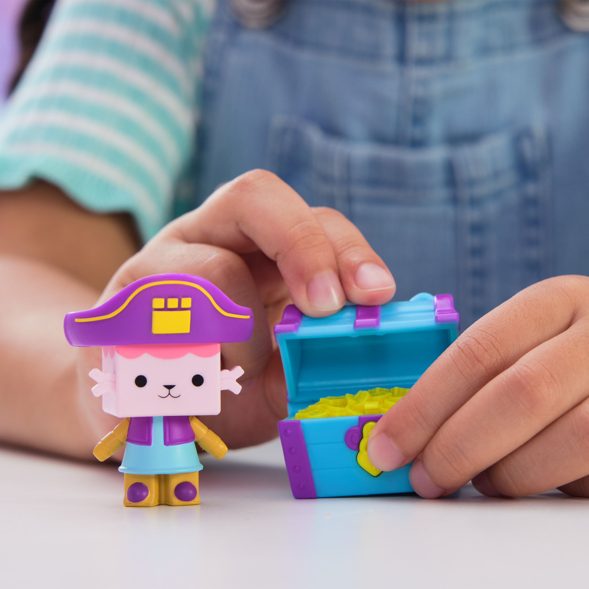 Manos de niño sostienen un pirata de juguete y un cofre del tesoro abierto sobre una superficie blanca.